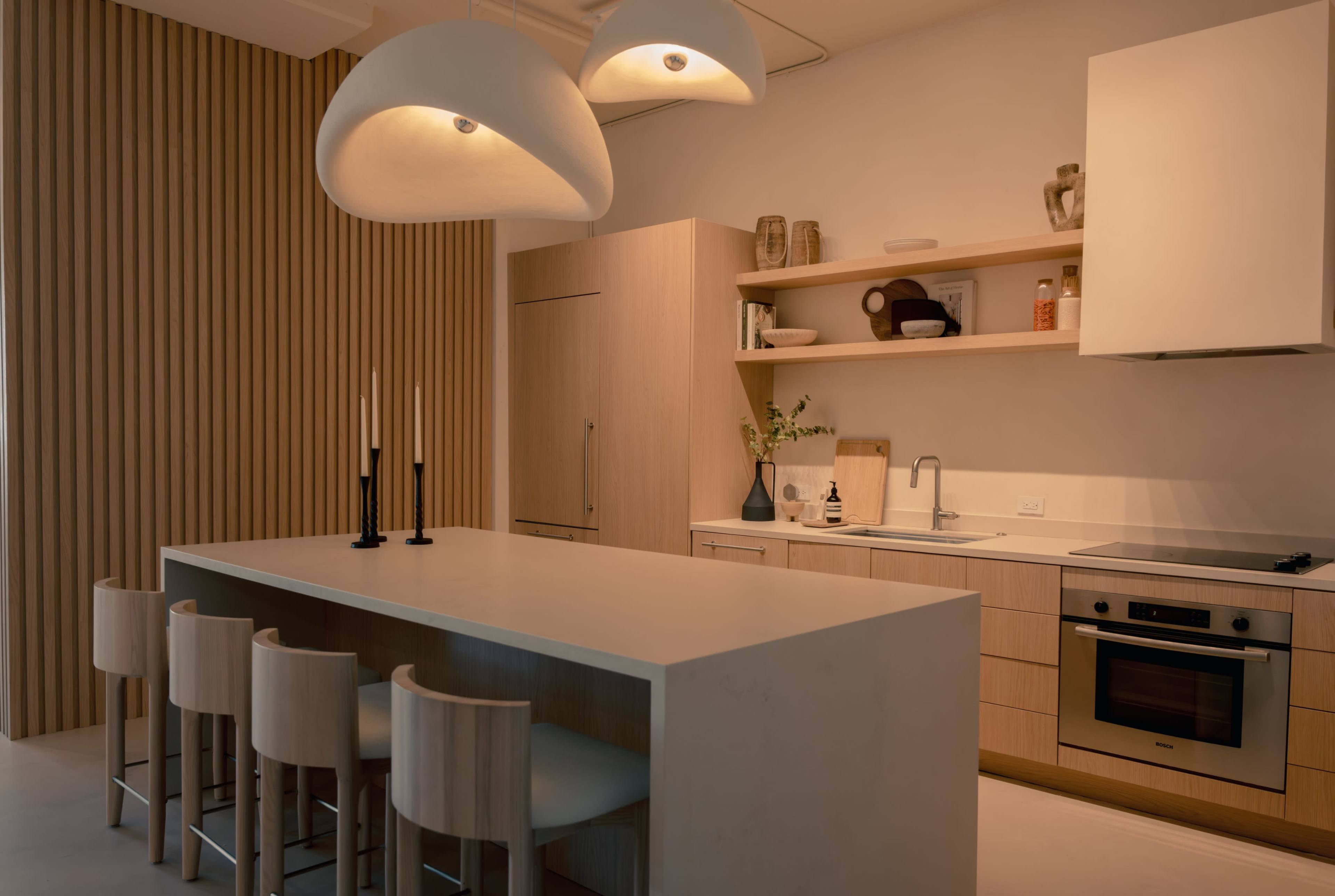 A modern kitchen features a long island with seating, wooden cabinetry, and pendant lights hanging from the ceiling.