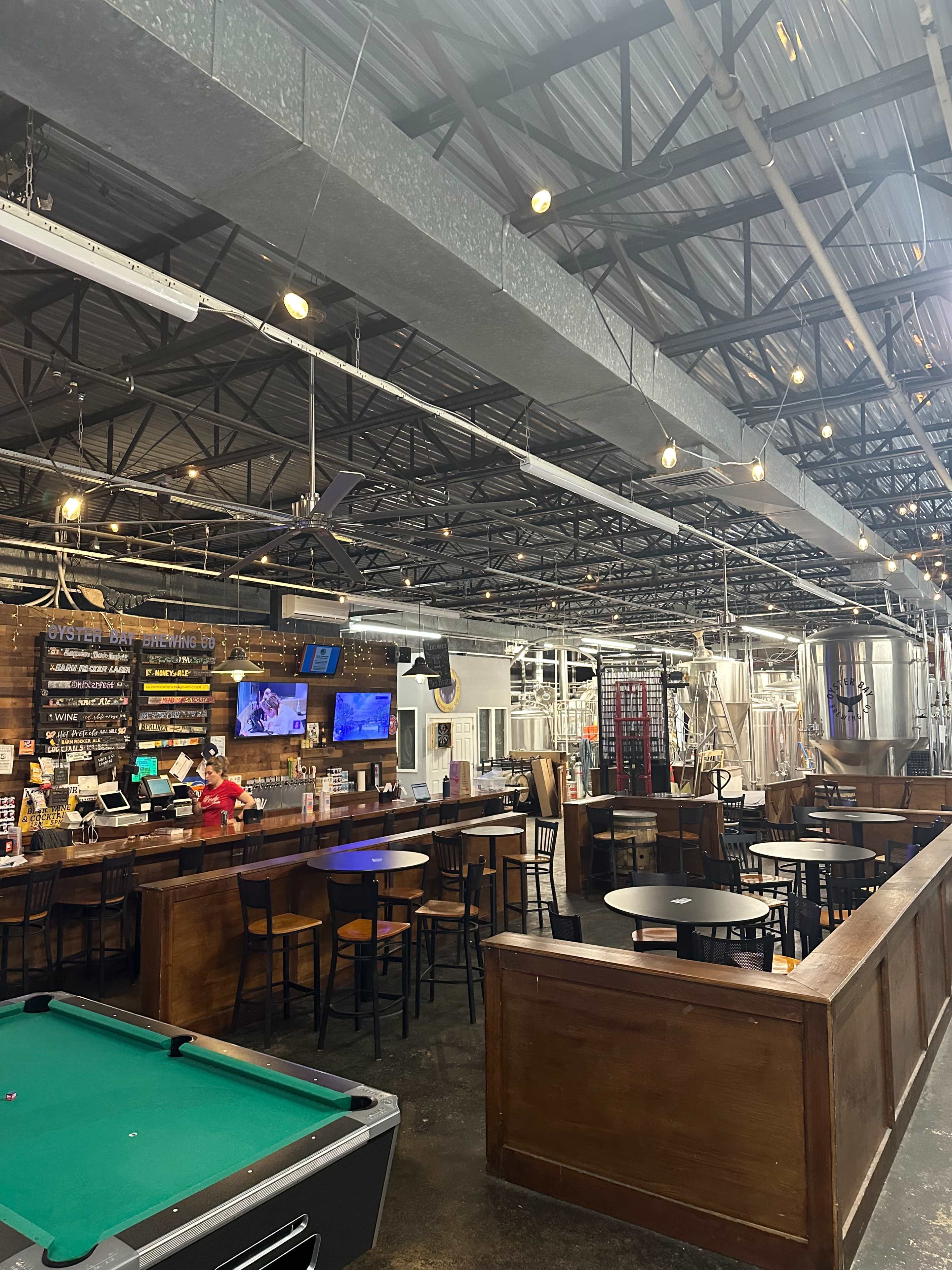 The image shows the interior of a bar or brewery with a pool table, bar counter, and various tables arranged beneath industrial-style lighting.
