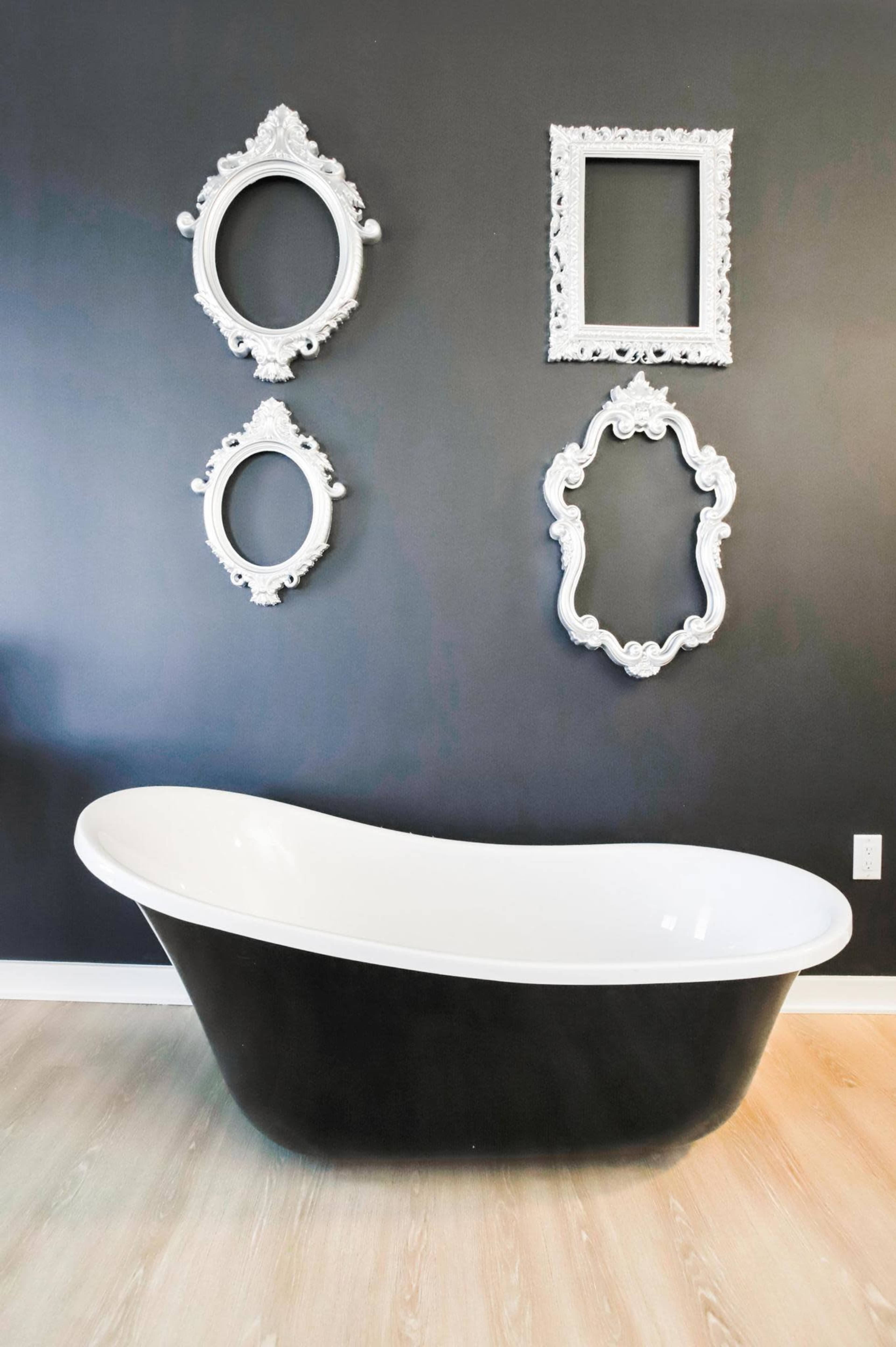 A black and white freestanding bathtub is positioned against a dark wall adorned with ornate white frames and mirrors.