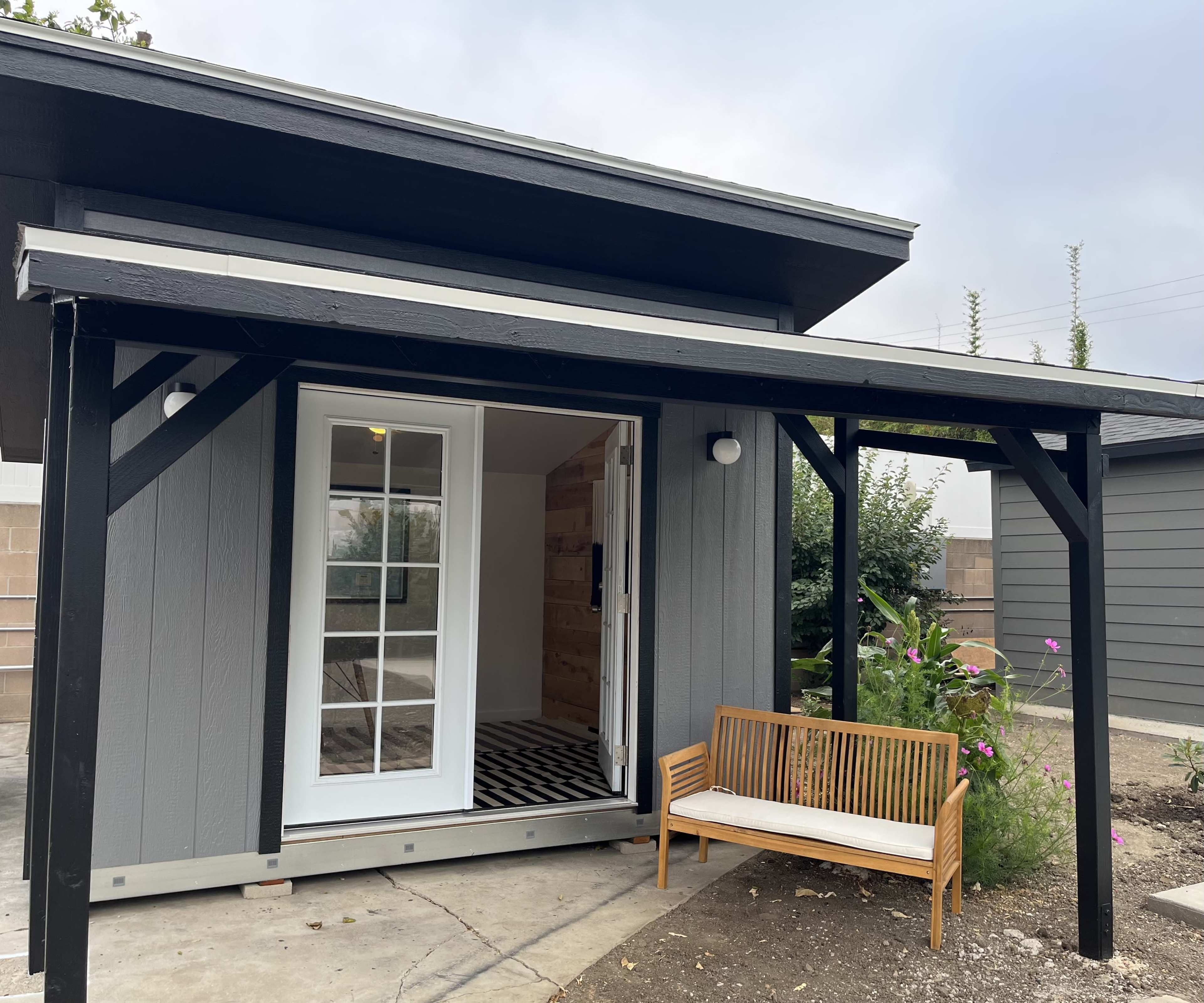 A modern gray house with a porch and a wooden bench sits in a landscaped area.