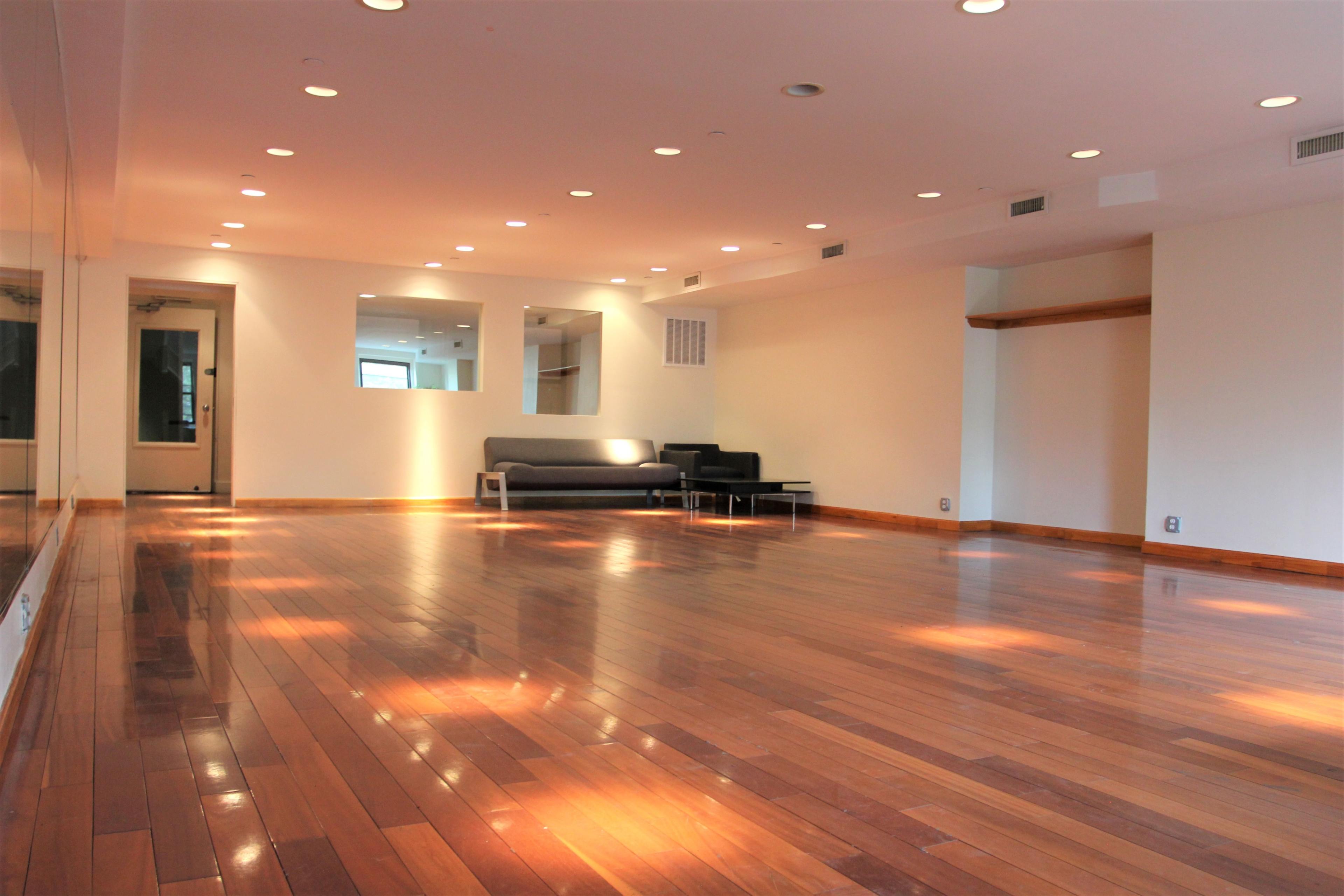 A spacious room with hardwood flooring, a gray sofa against the wall, and large mirrors reflecting the light.