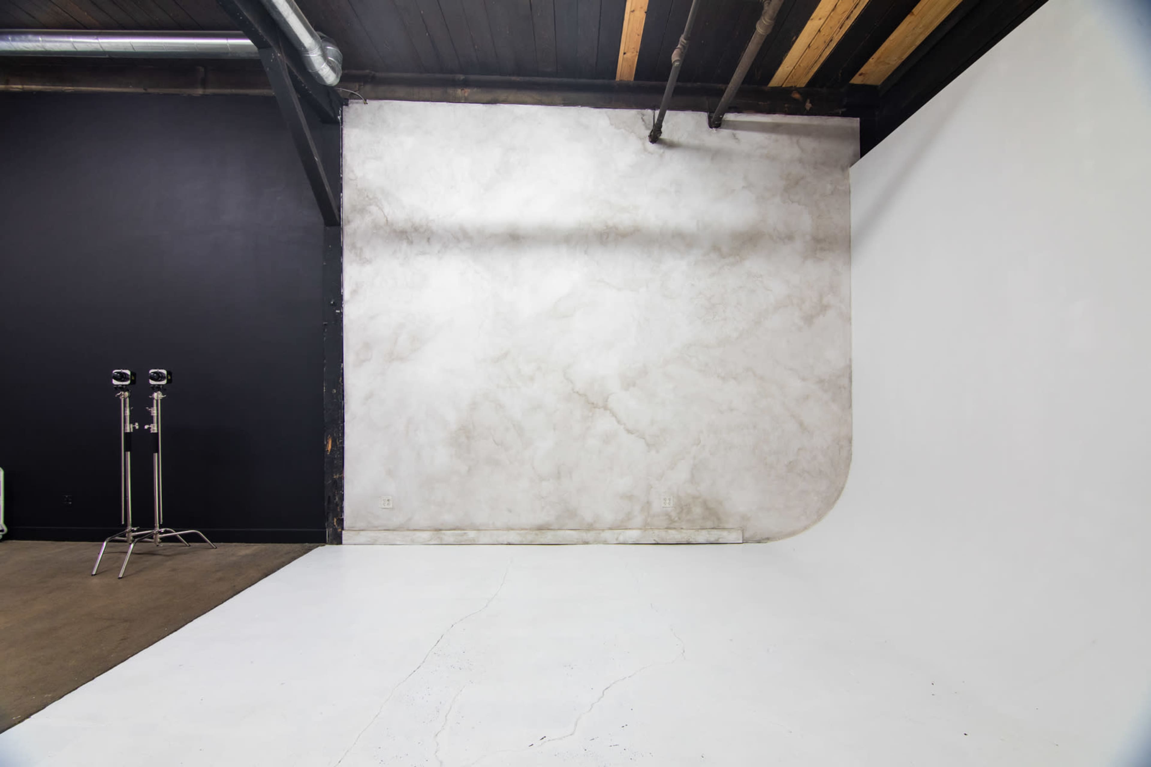 A photography studio with a curved white backdrop and a textured gray wall, illuminated by overhead lights.