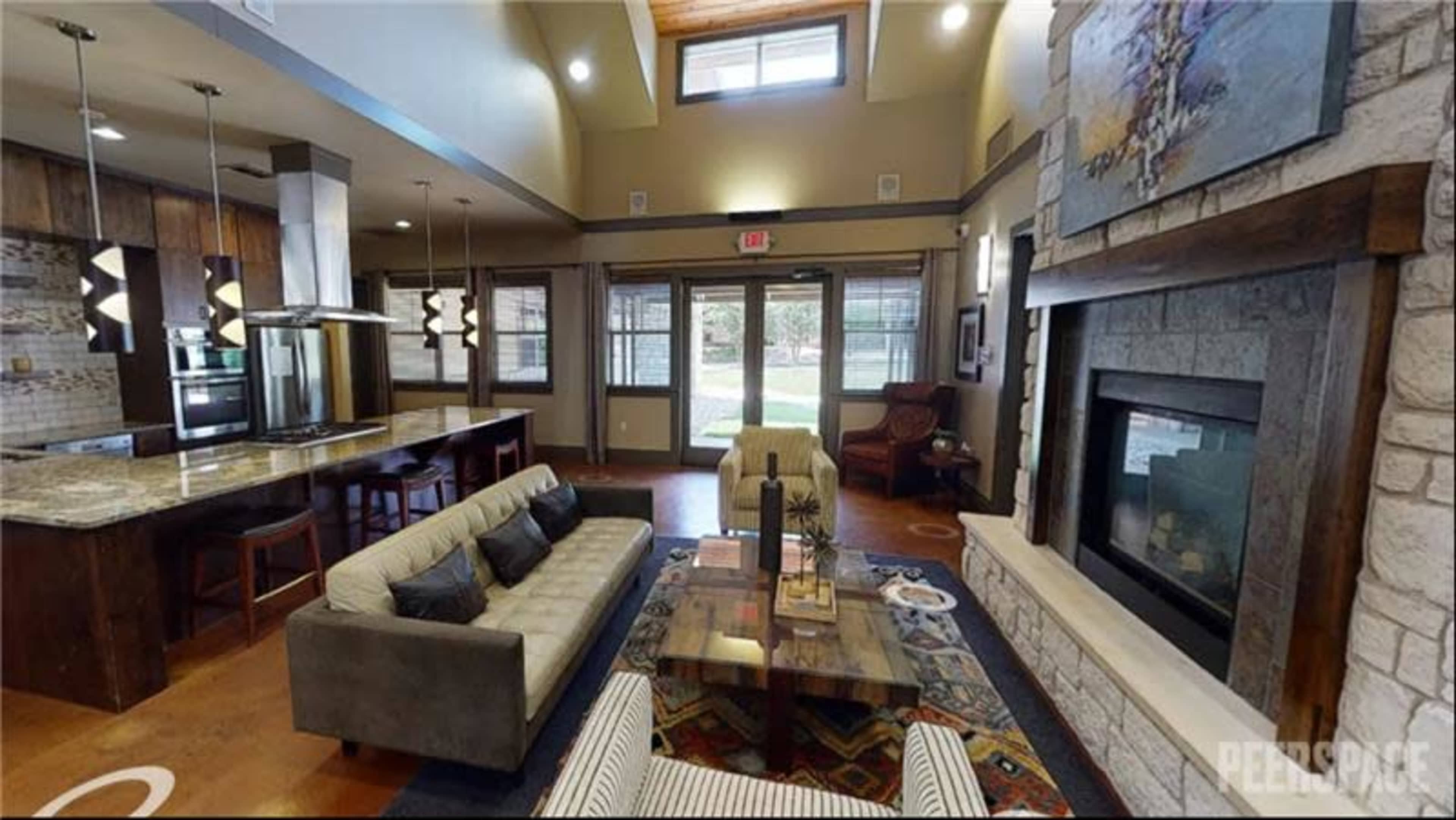 The image shows a modern lounge area featuring a sofa, coffee table, and a fireplace, with large windows allowing natural light and a view of the outside.