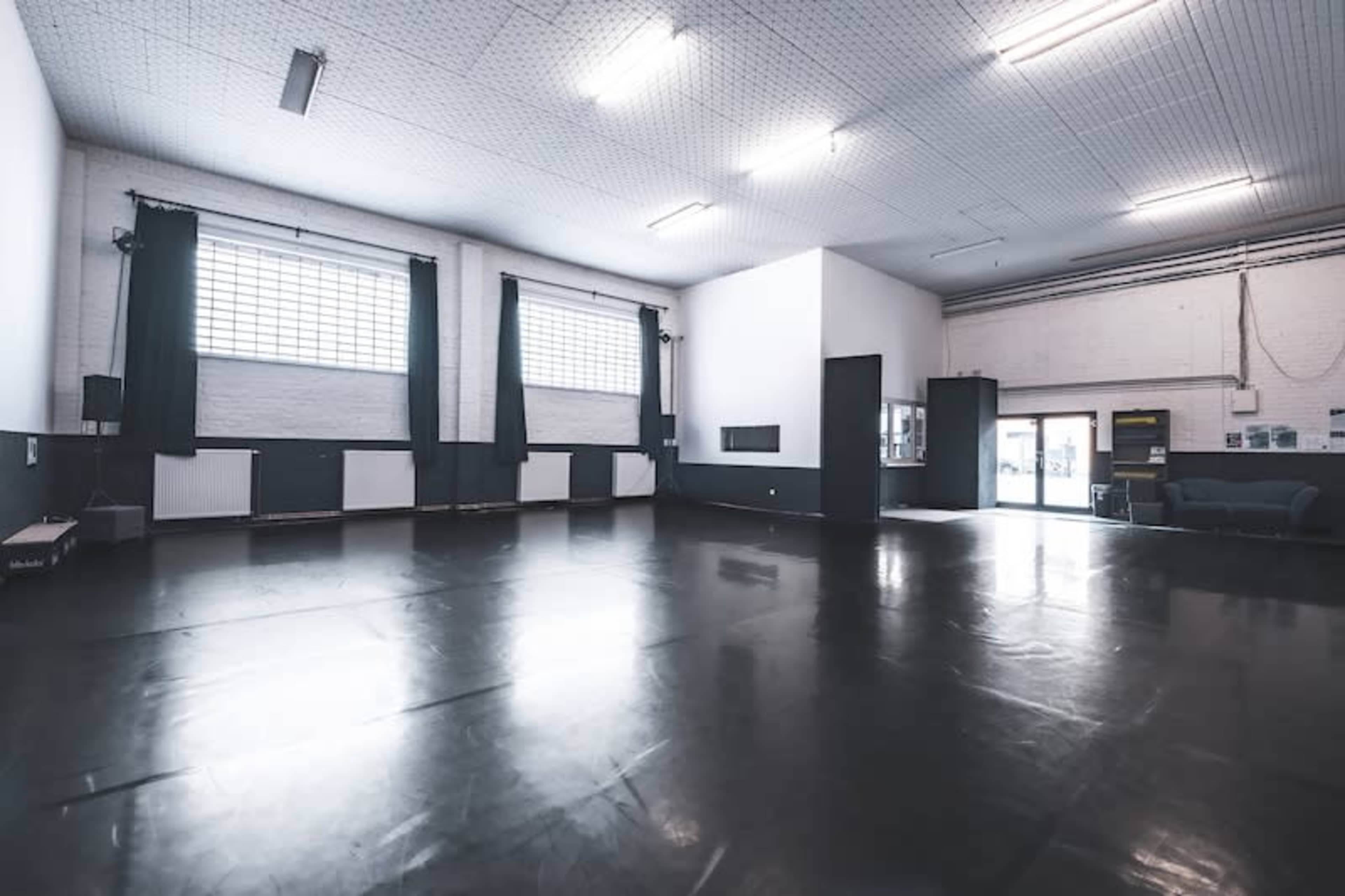 An empty dance studio with a dark floor, large windows, and white walls.