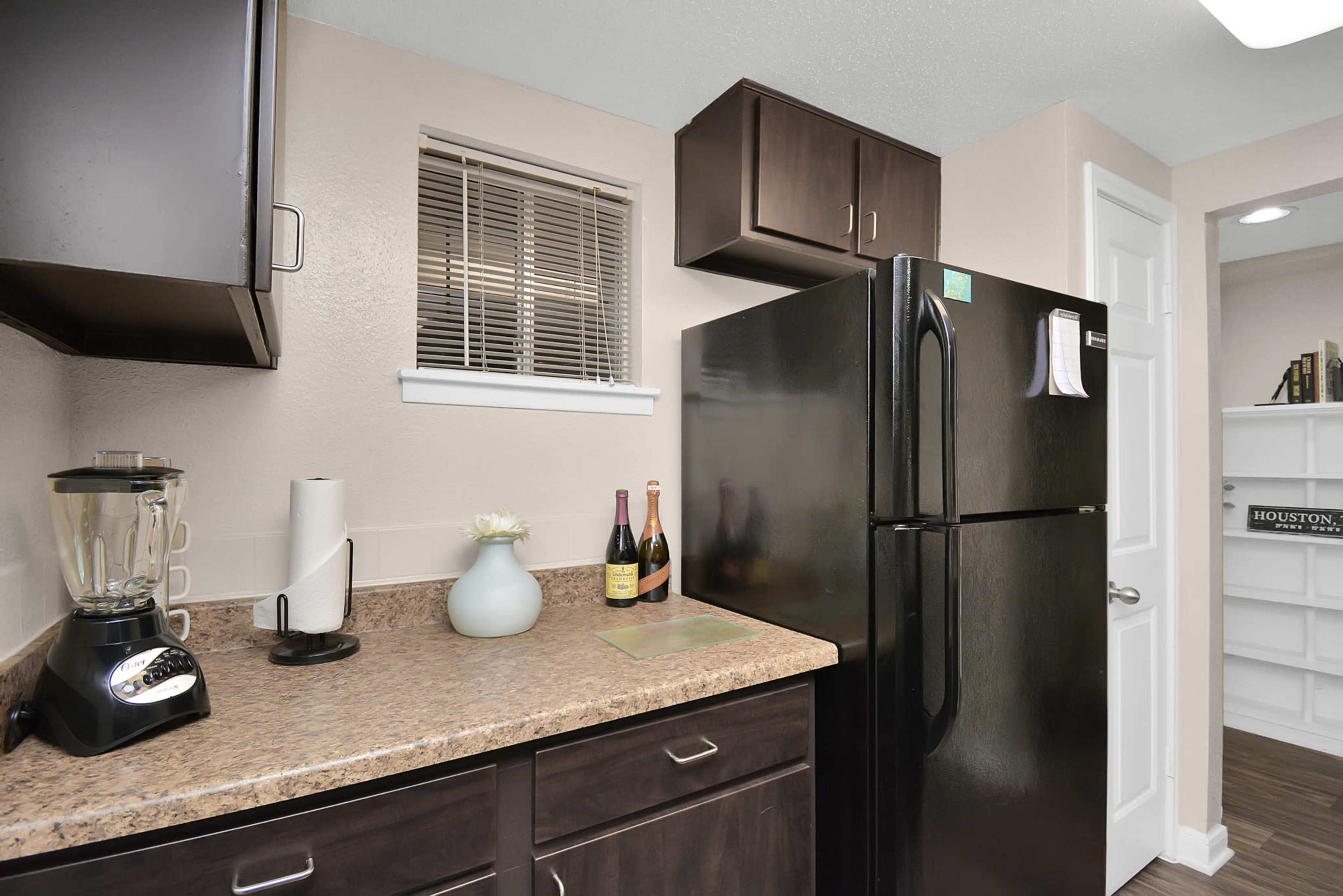 A kitchen space featuring dark wood cabinetry, a black refrigerator, a countertop with a blender, and a few decorative items.