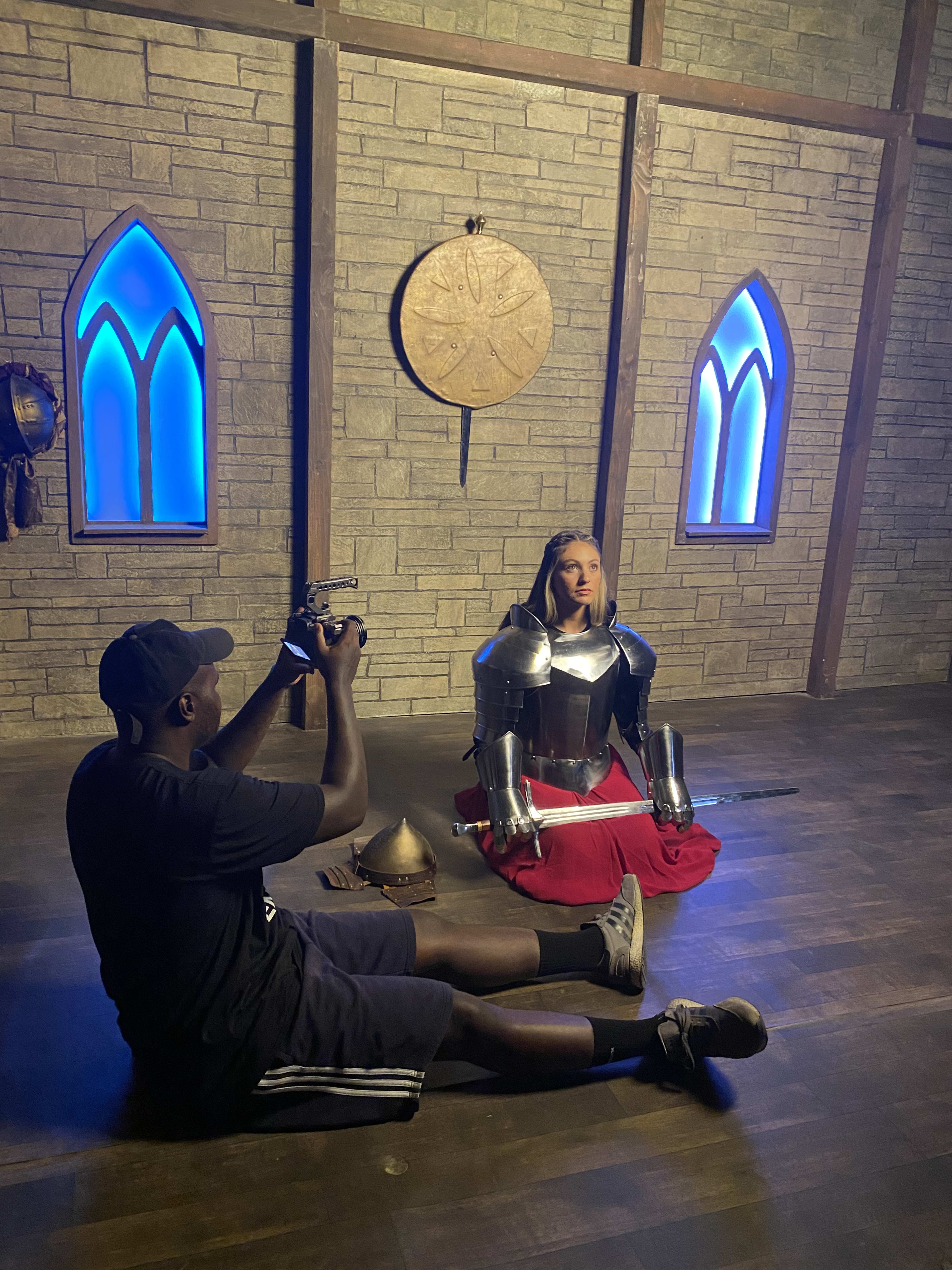 A man taking a picture of a sitting woman in a knight costume