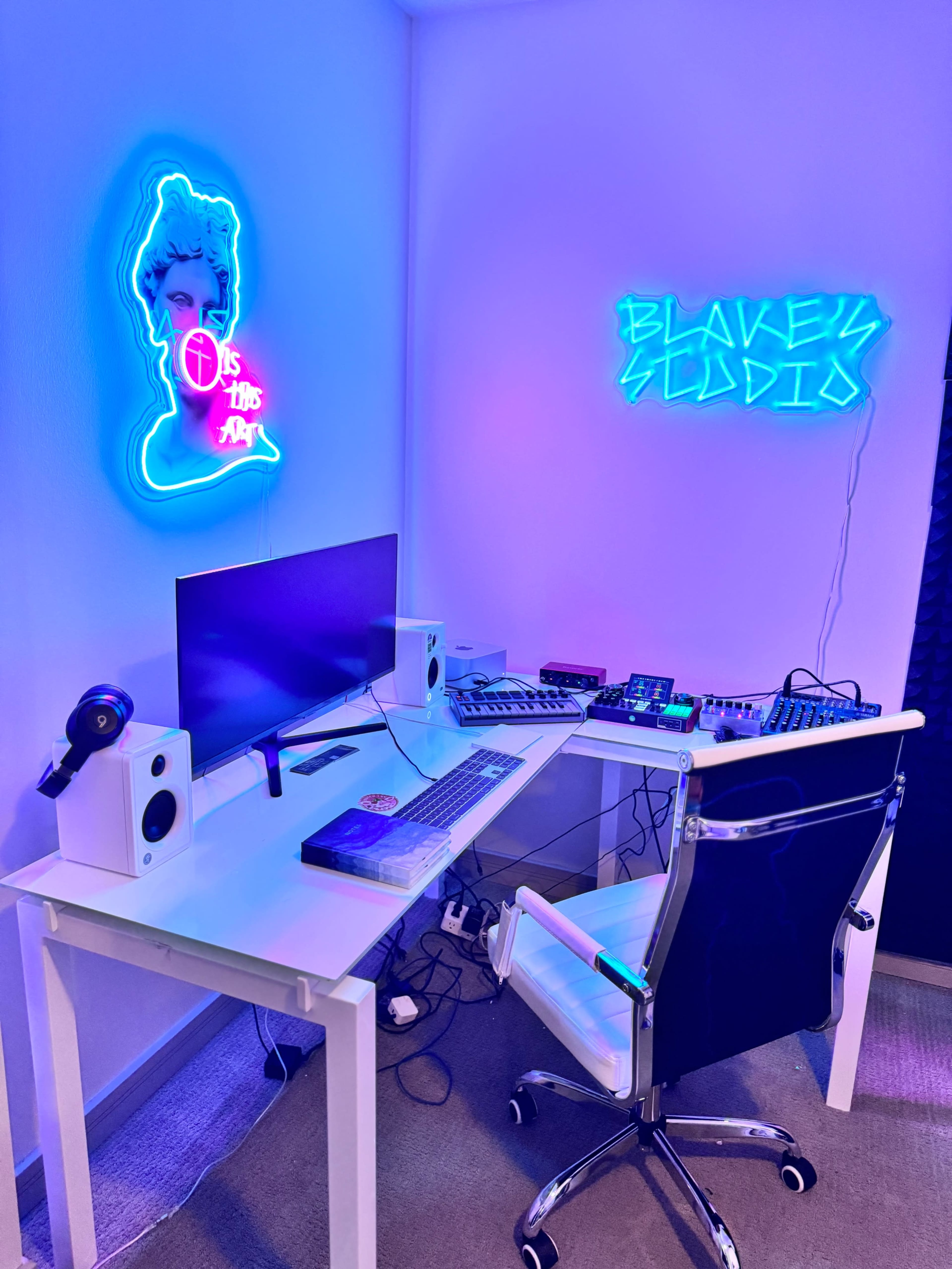 A modern desk setup features a computer monitor, musical equipment, and neon lights on the walls.