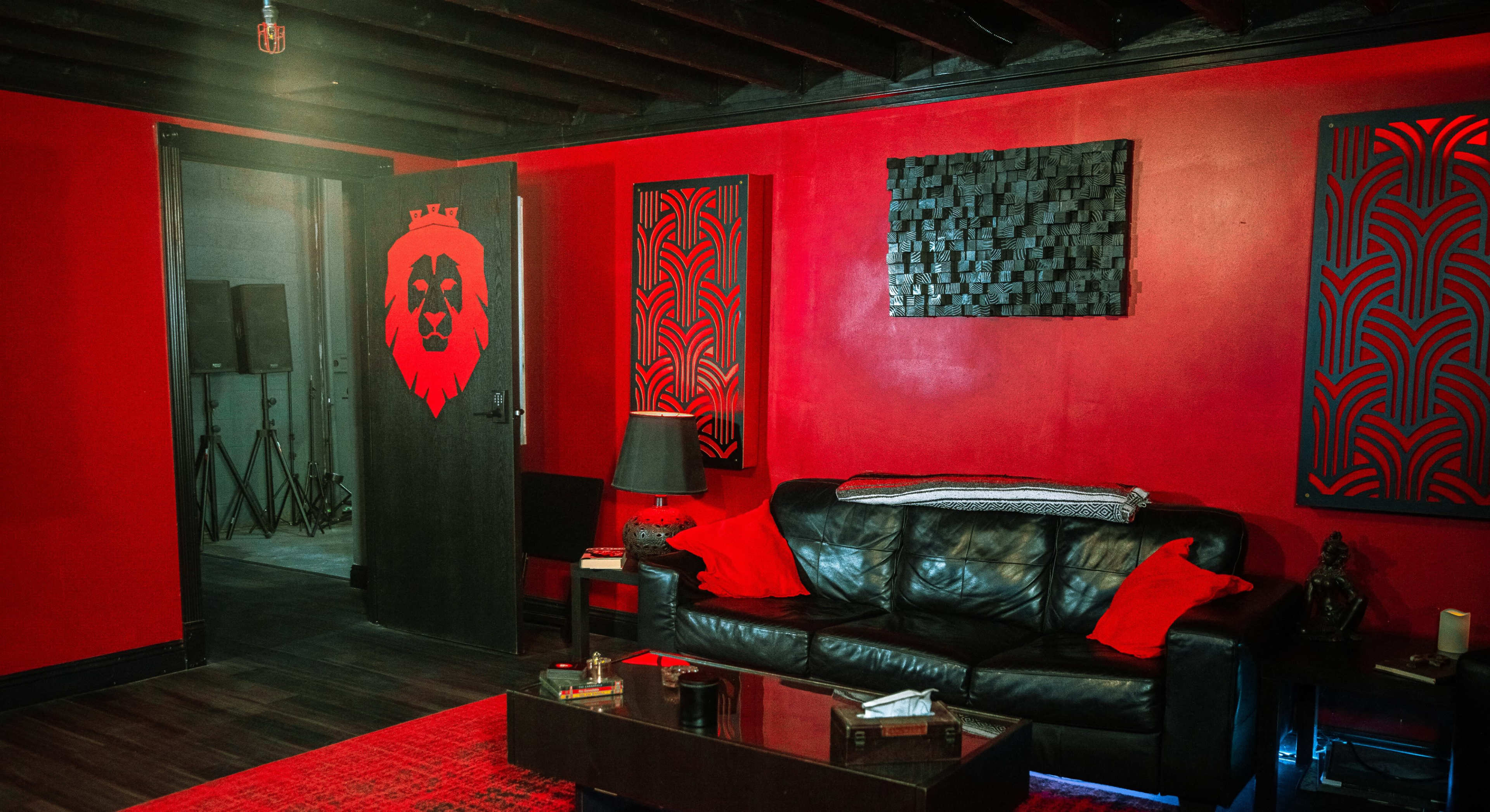 A room with red walls, a black leather sofa, and decorative elements including a lion emblem on the door and patterned wall art.