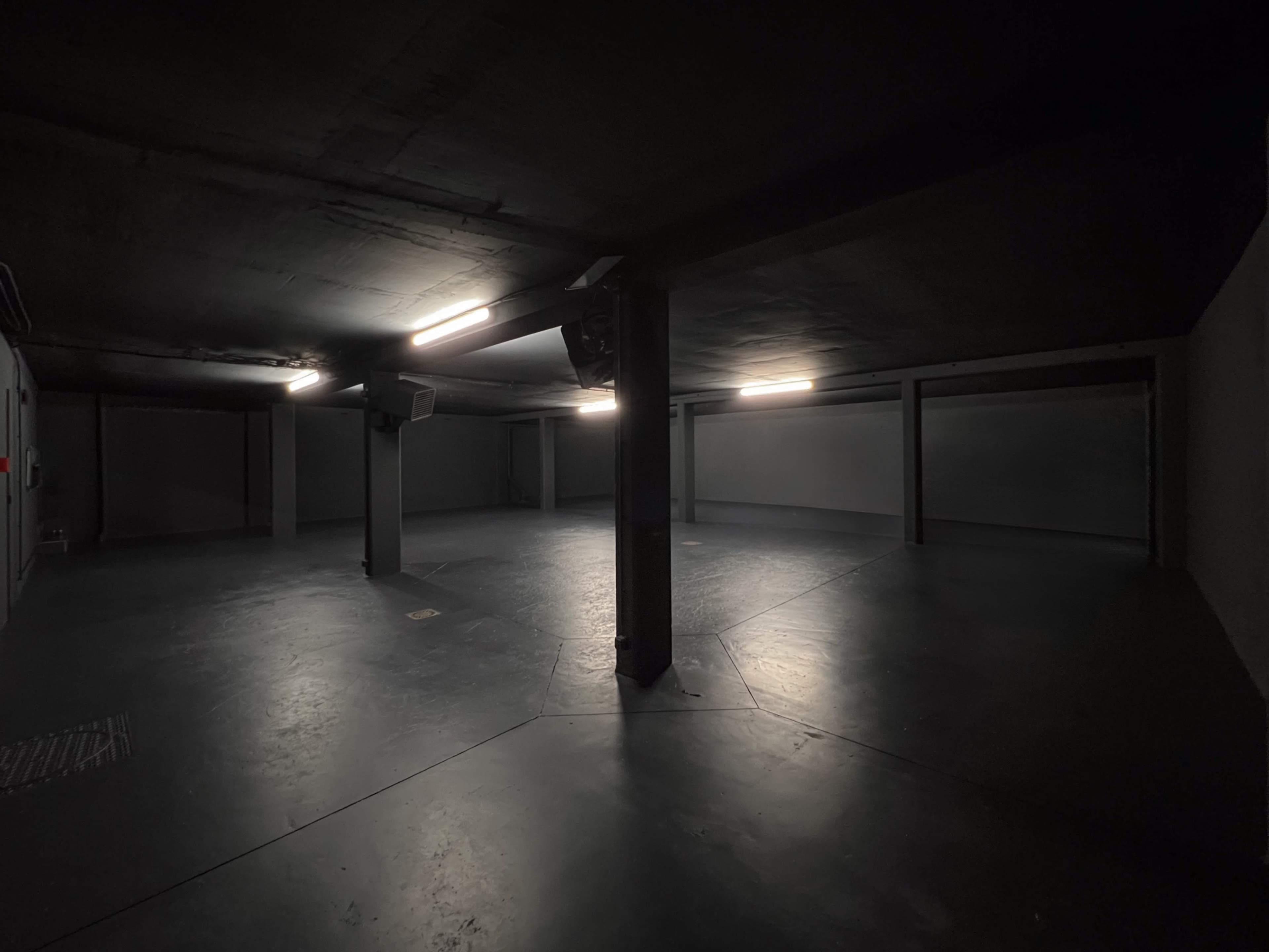 The image shows a dark parking garage with concrete walls and ceiling, illuminated by ceiling lights.