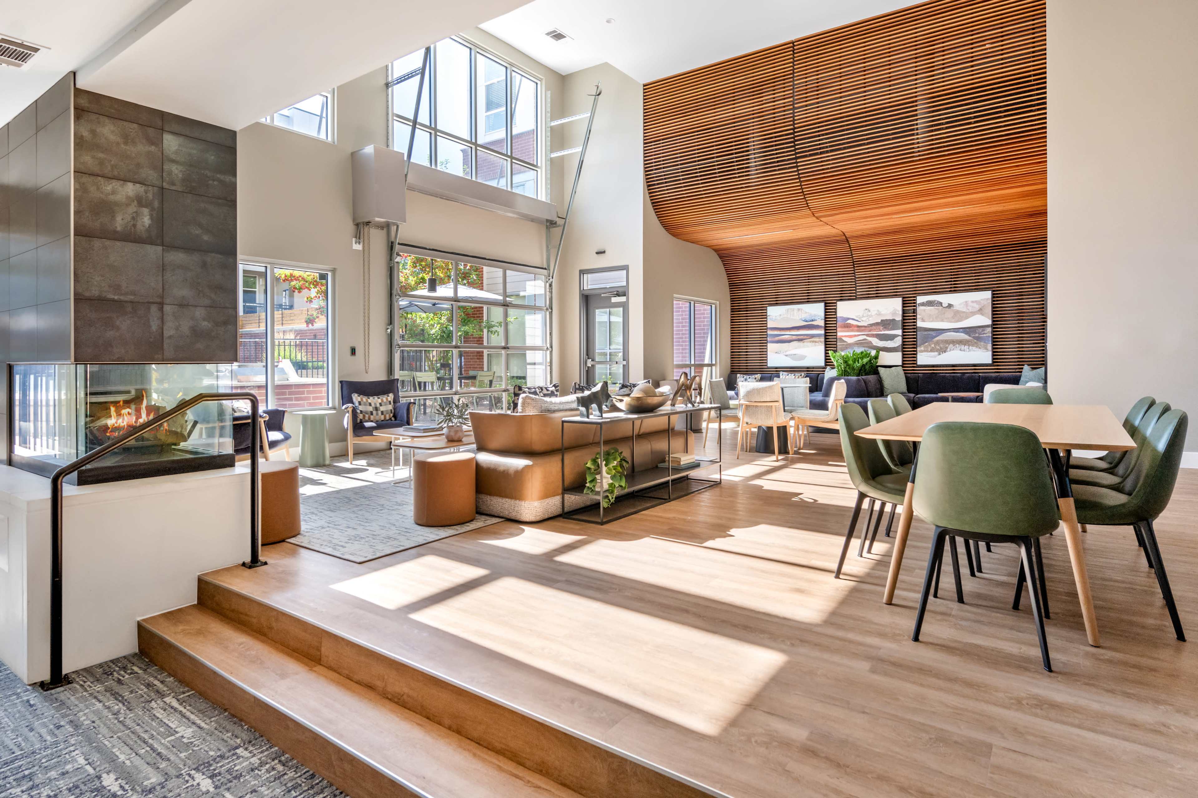 The spacious interior features large windows, a fireplace, modern seating arrangements, and a dining area with a wooden table, all set in a well-lit, contemporary design.