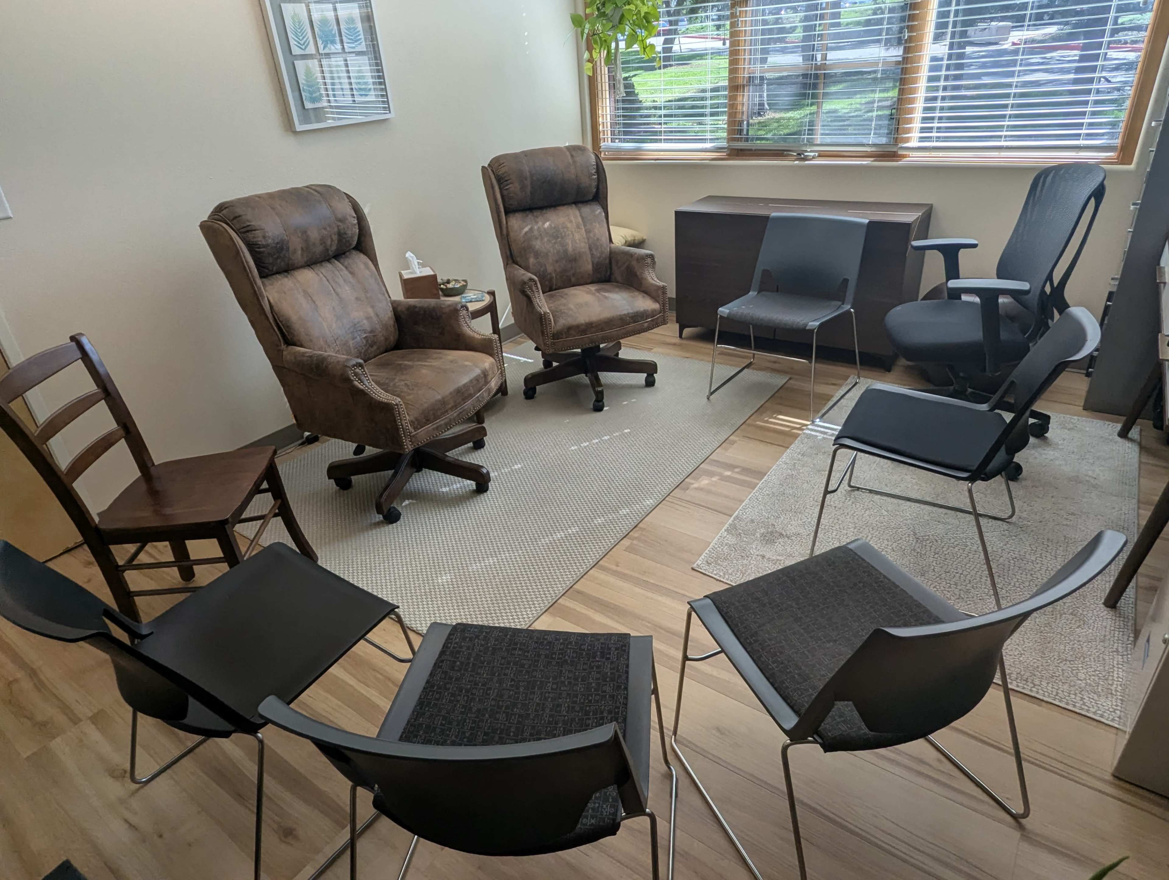 The image shows a seating arrangement of several chairs, including two recliners and multiple metal chairs, arranged in a circular formation on a carpeted floor.