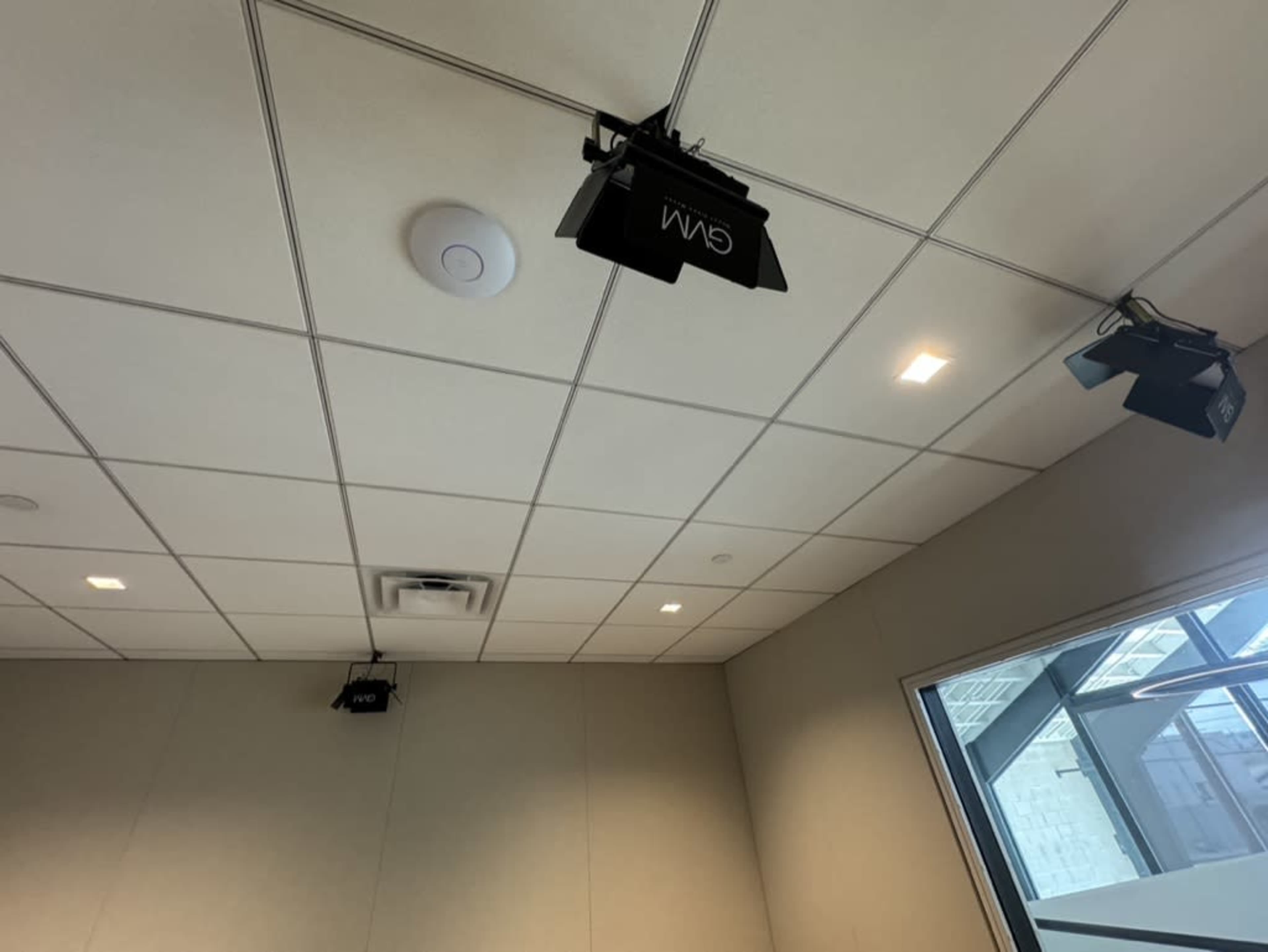 The image shows a ceiling with recessed lights and several mounted lights, along with a circular panel, in a room with a window.