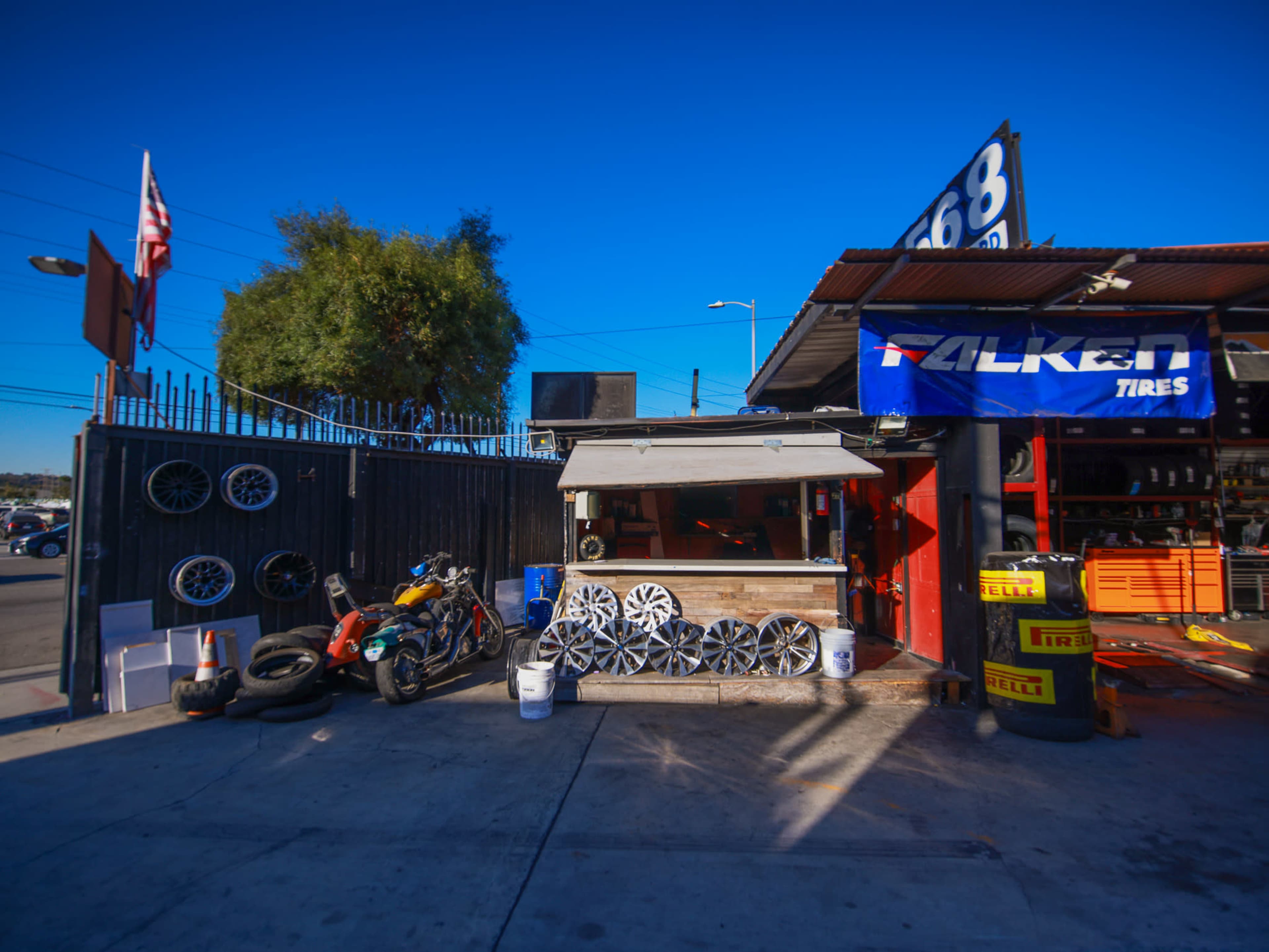 The image shows a tire shop with a selection of wheels and tires displayed outside, along with tools and equipment.