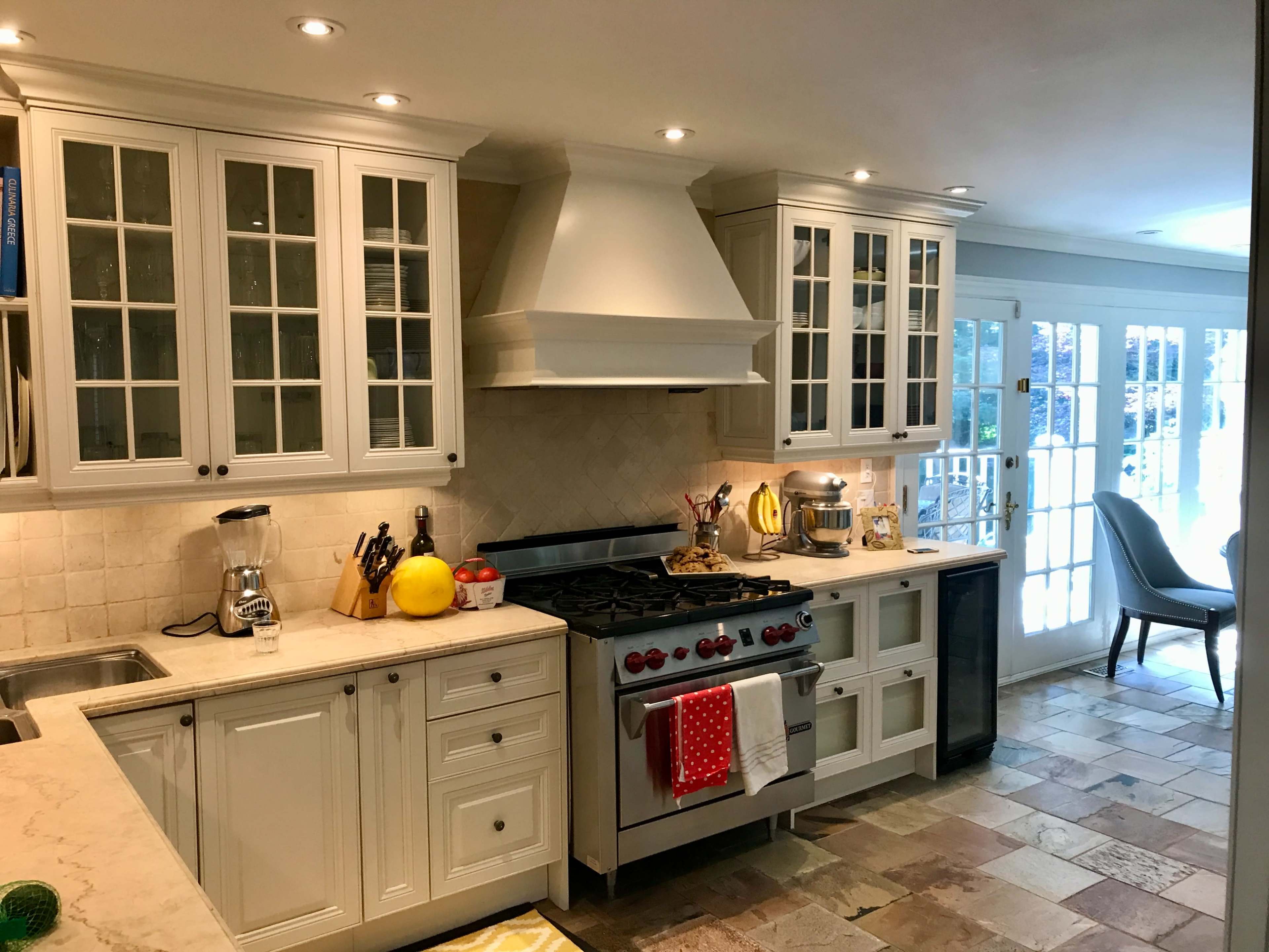The image shows a modern kitchen with white cabinetry, a large stainless steel stove, and a stone tile floor.