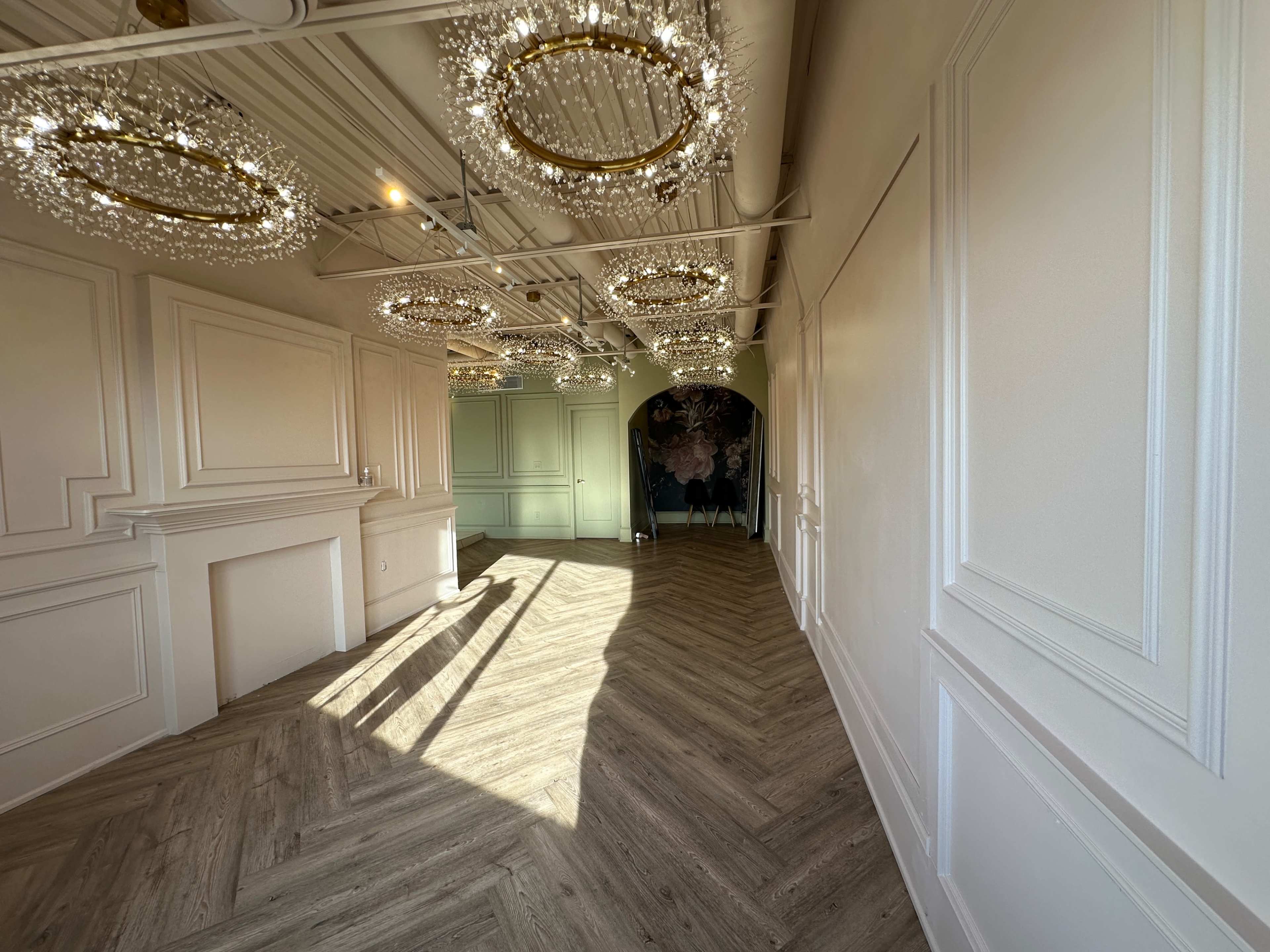 An elegantly designed interior space with herringbone-patterned flooring and decorative chandeliers hanging from the ceiling.