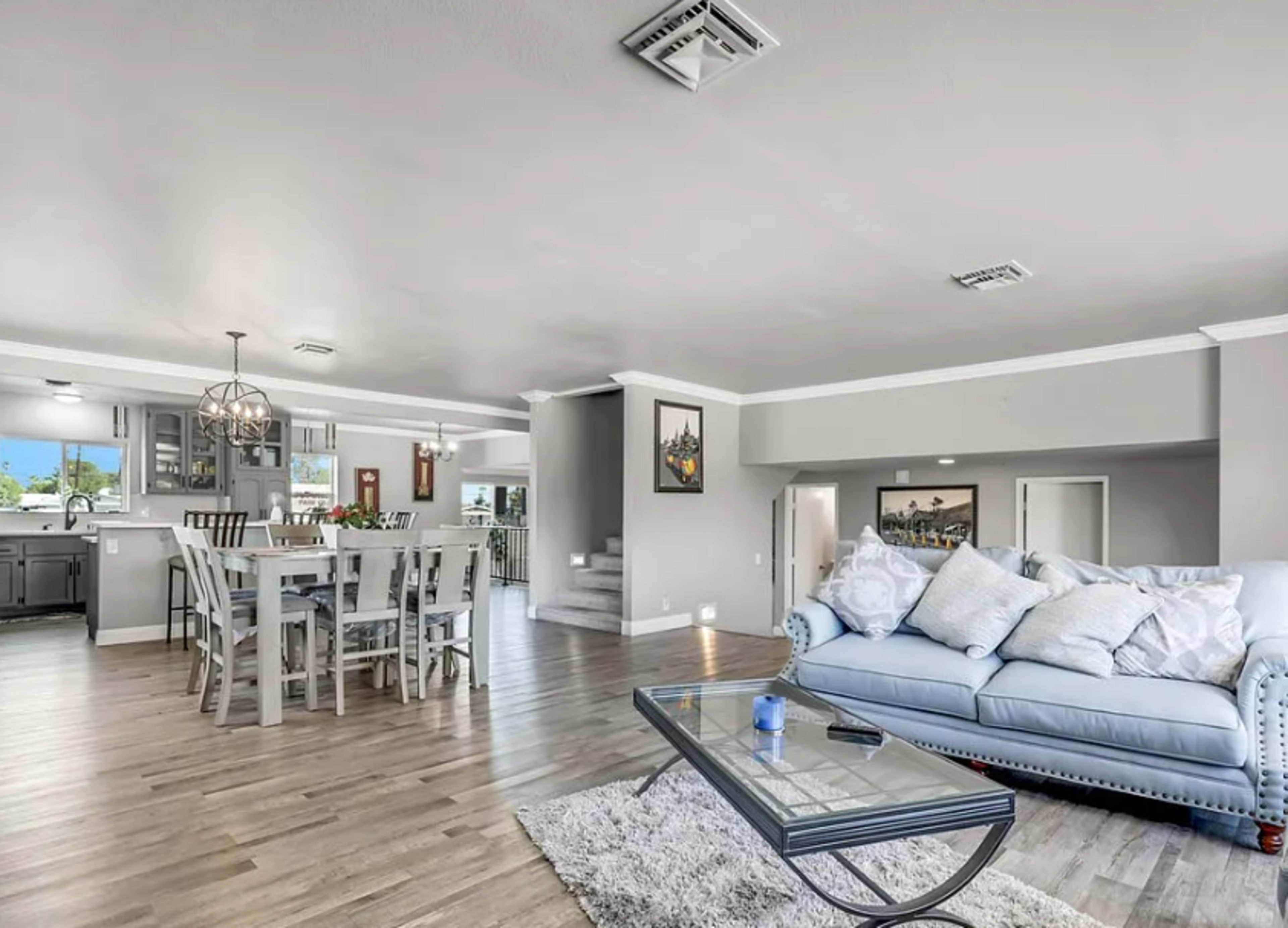 The image shows an open-concept living and dining area with a light blue couch, a glass coffee table, and a dining table surrounded by chairs.