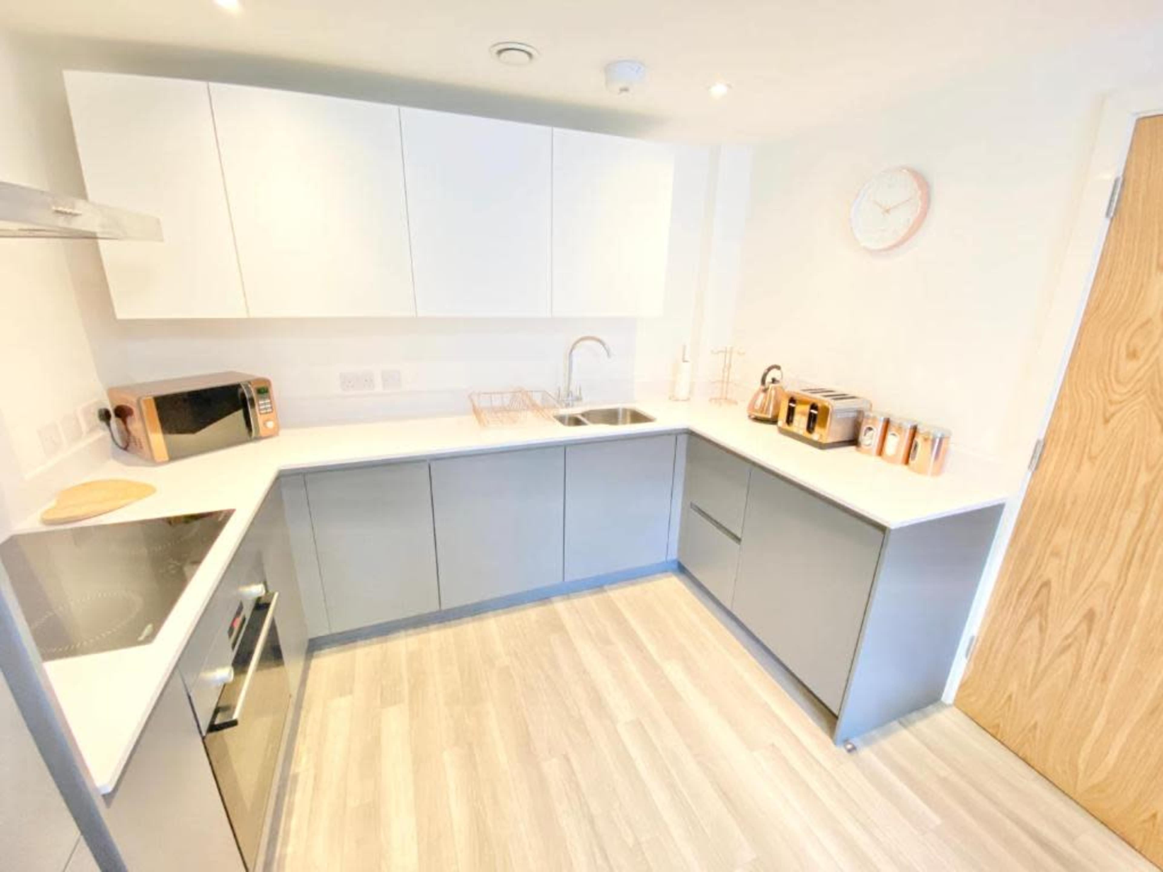 A modern kitchen with light gray and white cabinetry, a sink, a microwave, and several kitchen appliances neatly arranged on the counter.