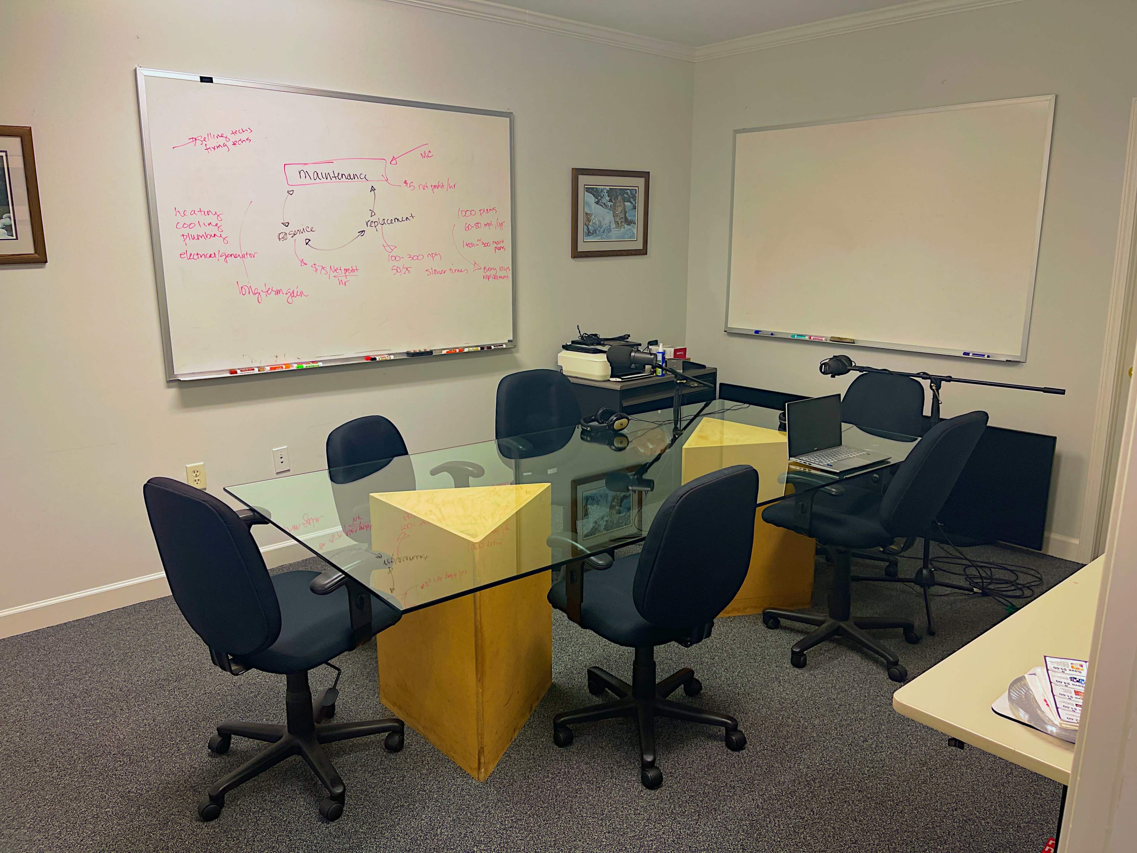 A conference room features a glass table with yellow pedestals, surrounded by black chairs, and a whiteboard filled with notes on one wall.