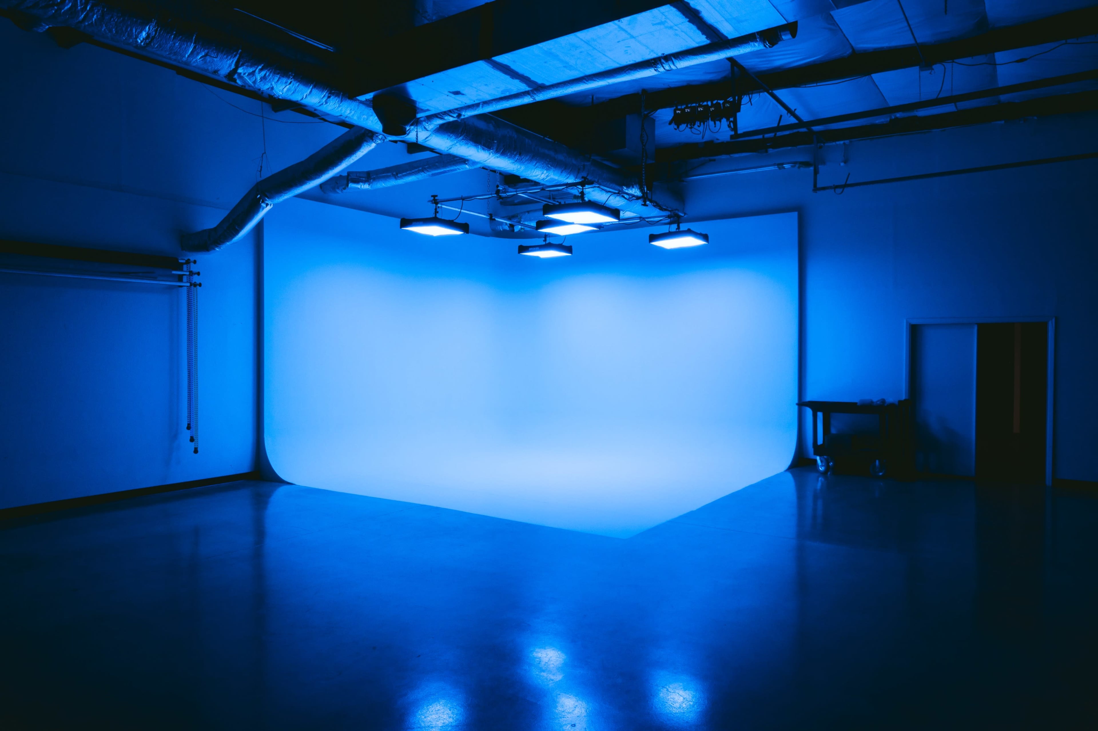 The image shows an empty studio space illuminated by blue lighting, featuring a seamless background and polished floor.