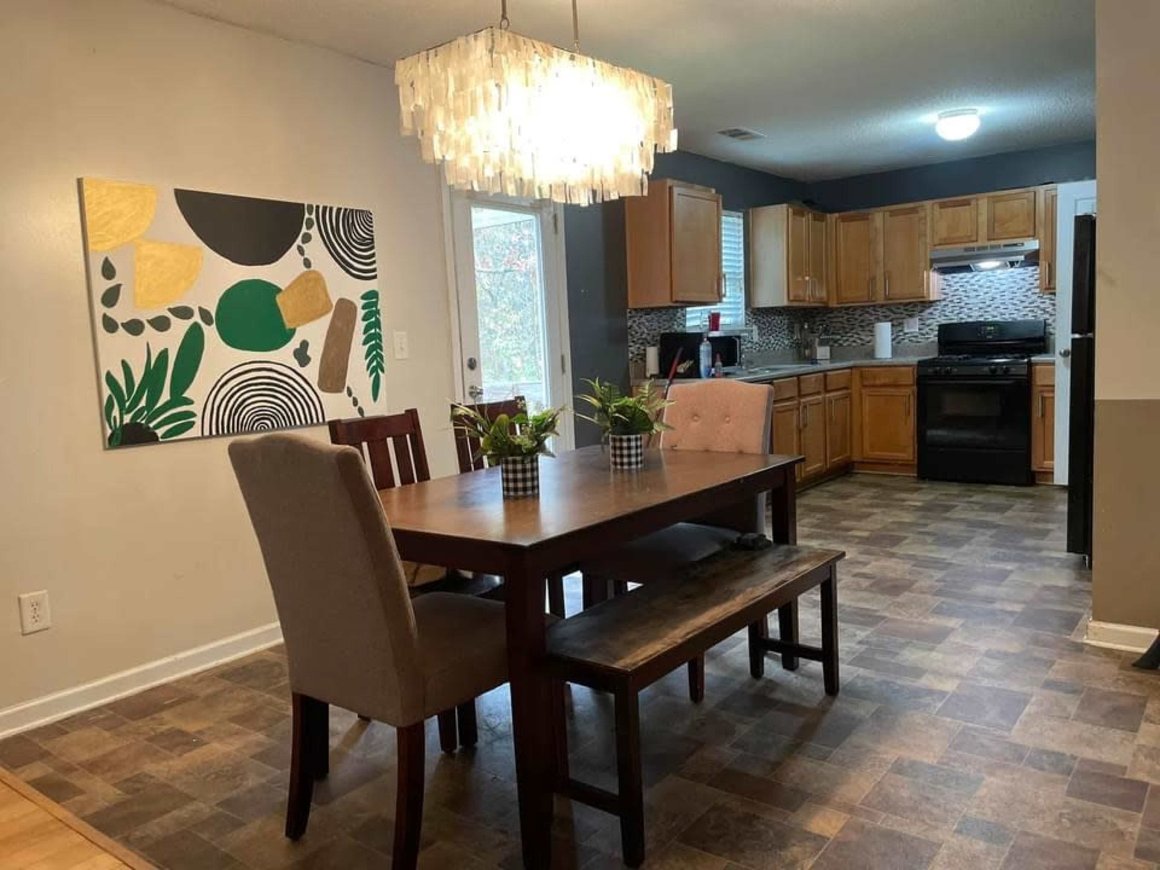 A dining area features a wooden table with seating, surrounded by a modern kitchen with cabinets and a patterned backsplash.