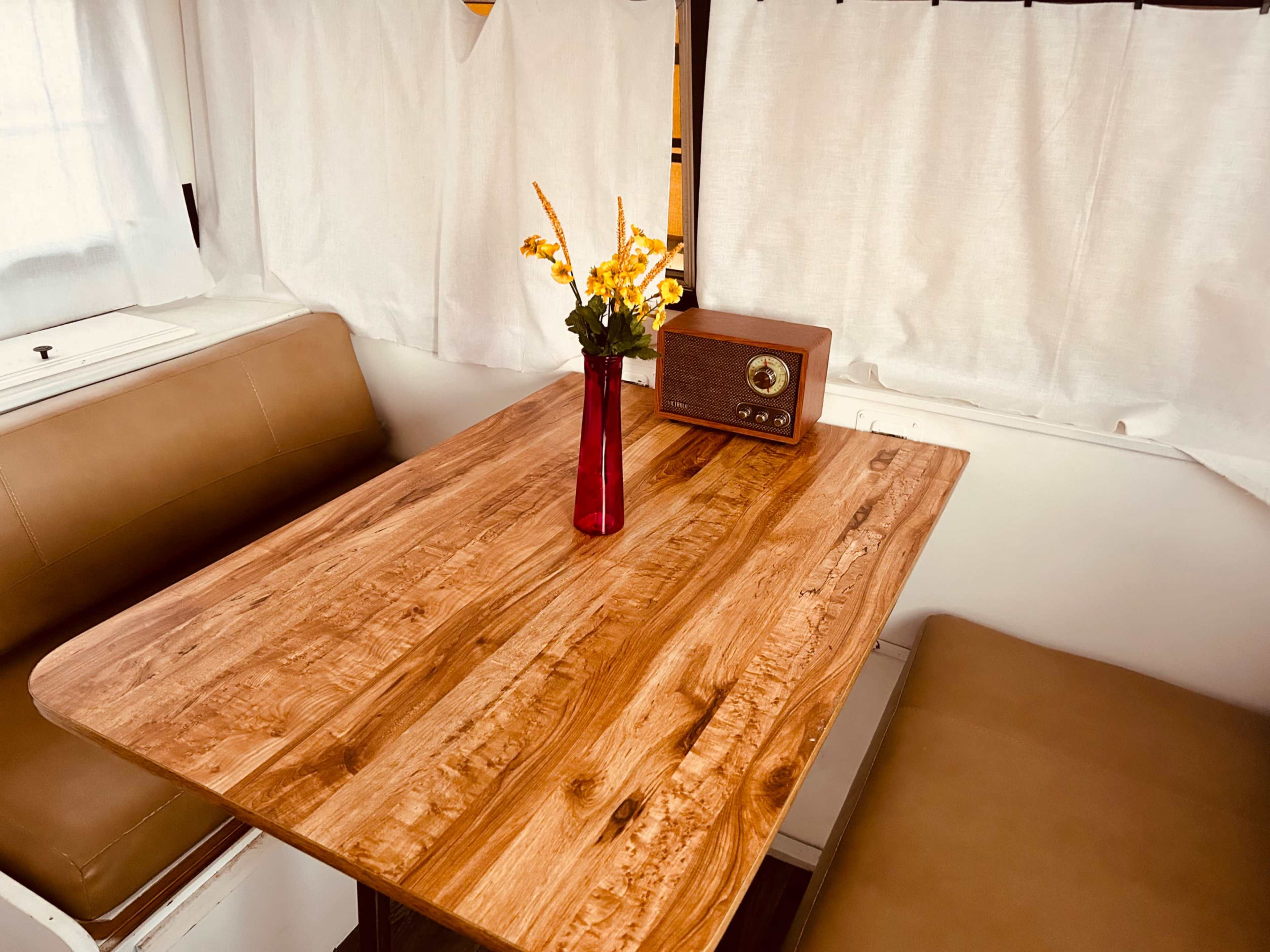 A wooden table with a red vase containing yellow flowers sits next to a vintage radio in a brightly lit interior.