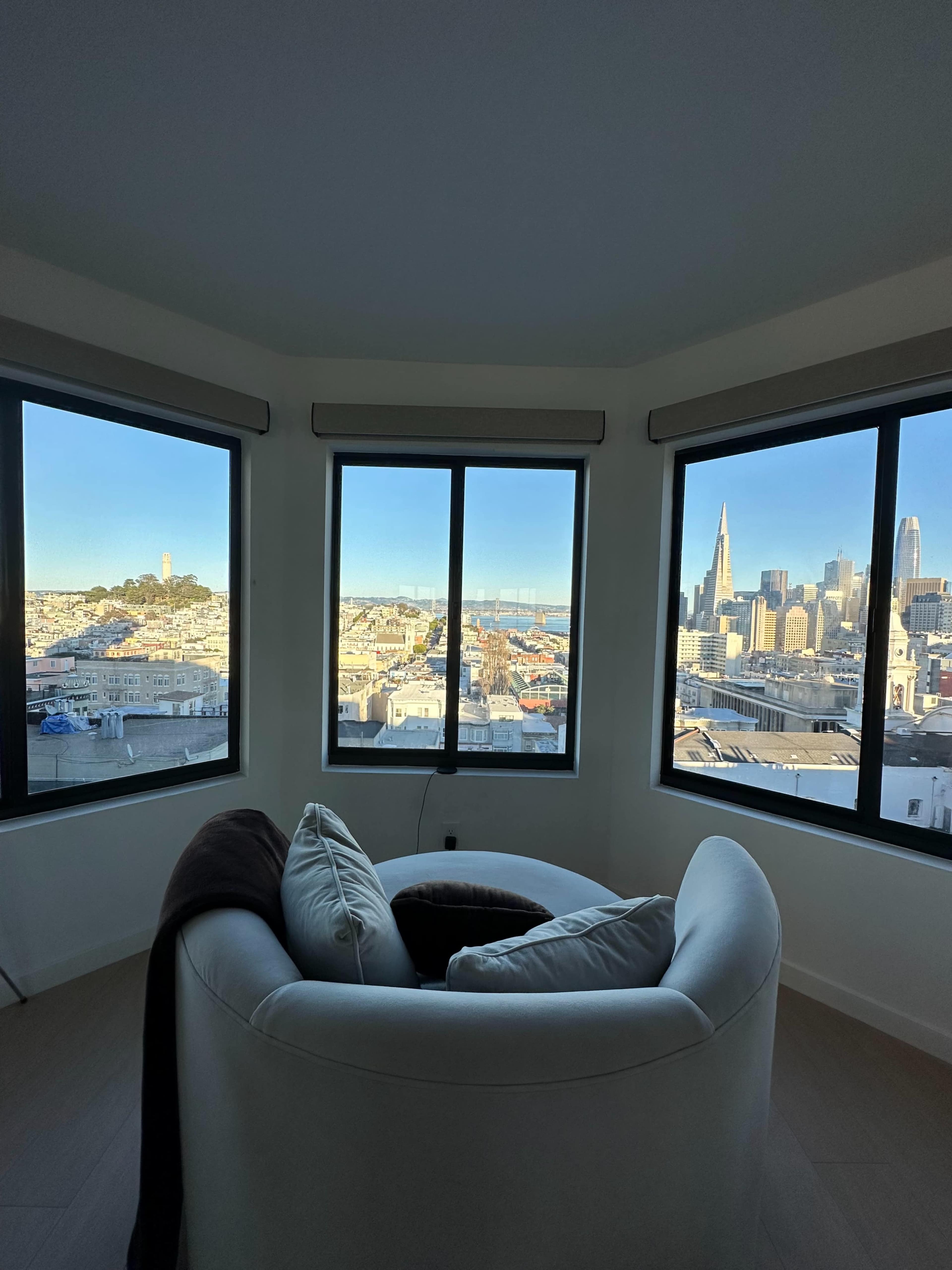 A cozy white armchair positioned in a bay window with a panoramic view of a city skyline and landmarks.