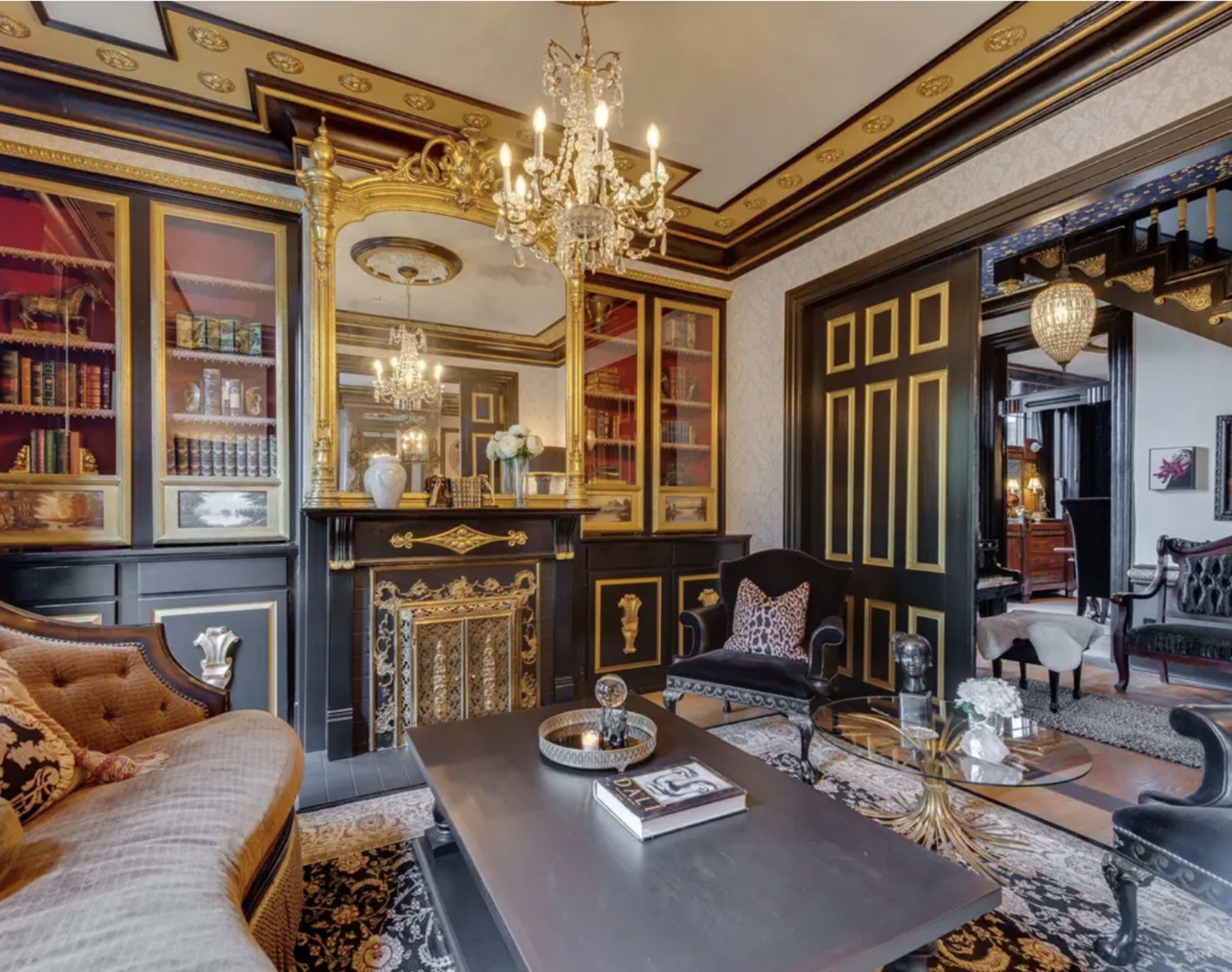 A luxurious living room featuring ornate gold accents, a decorative fireplace, and a variety of books displayed in glass-fronted cabinets.
