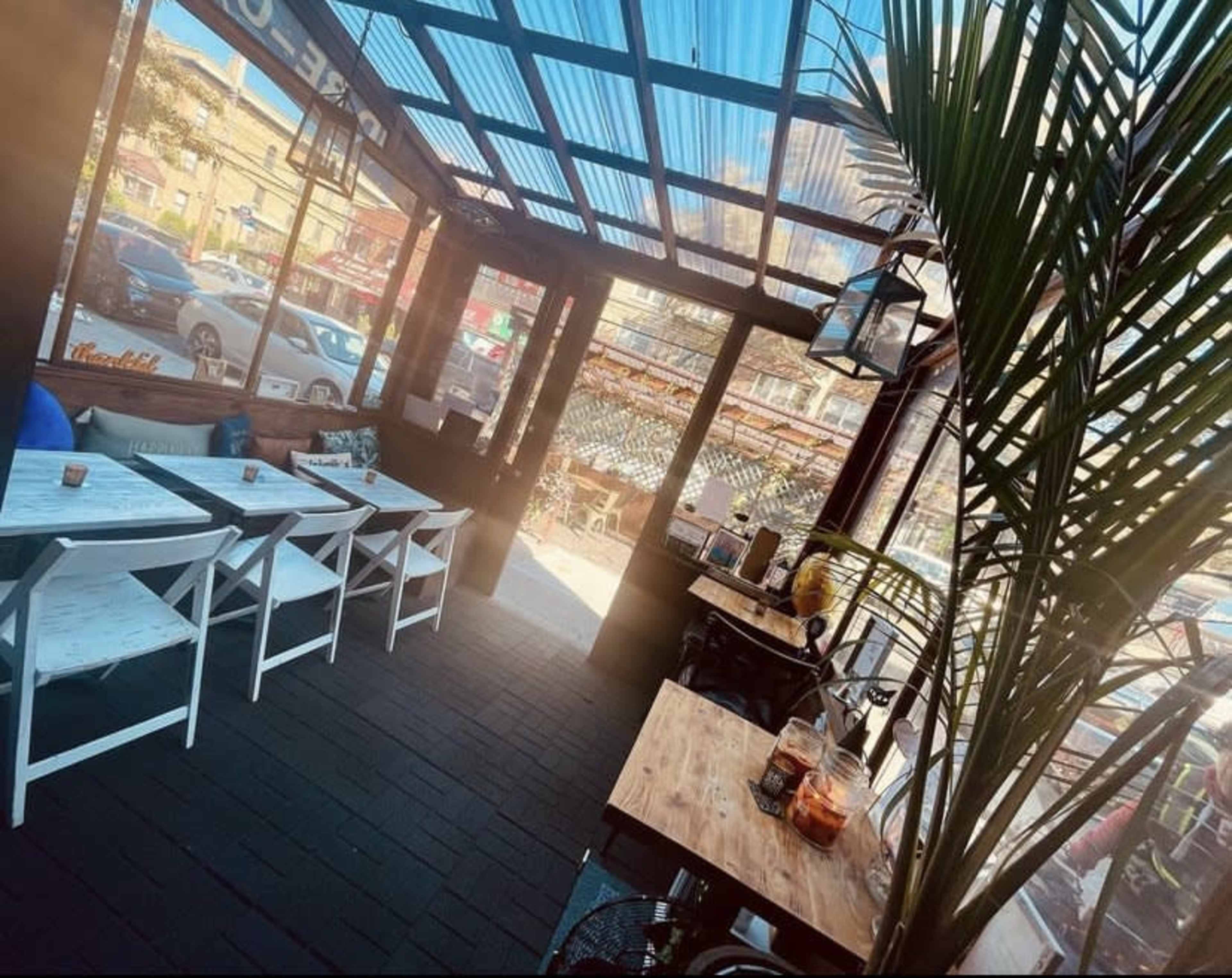 A sunlit indoor space of a café with wooden tables, white chairs, and large windows overlooking a bustling street.