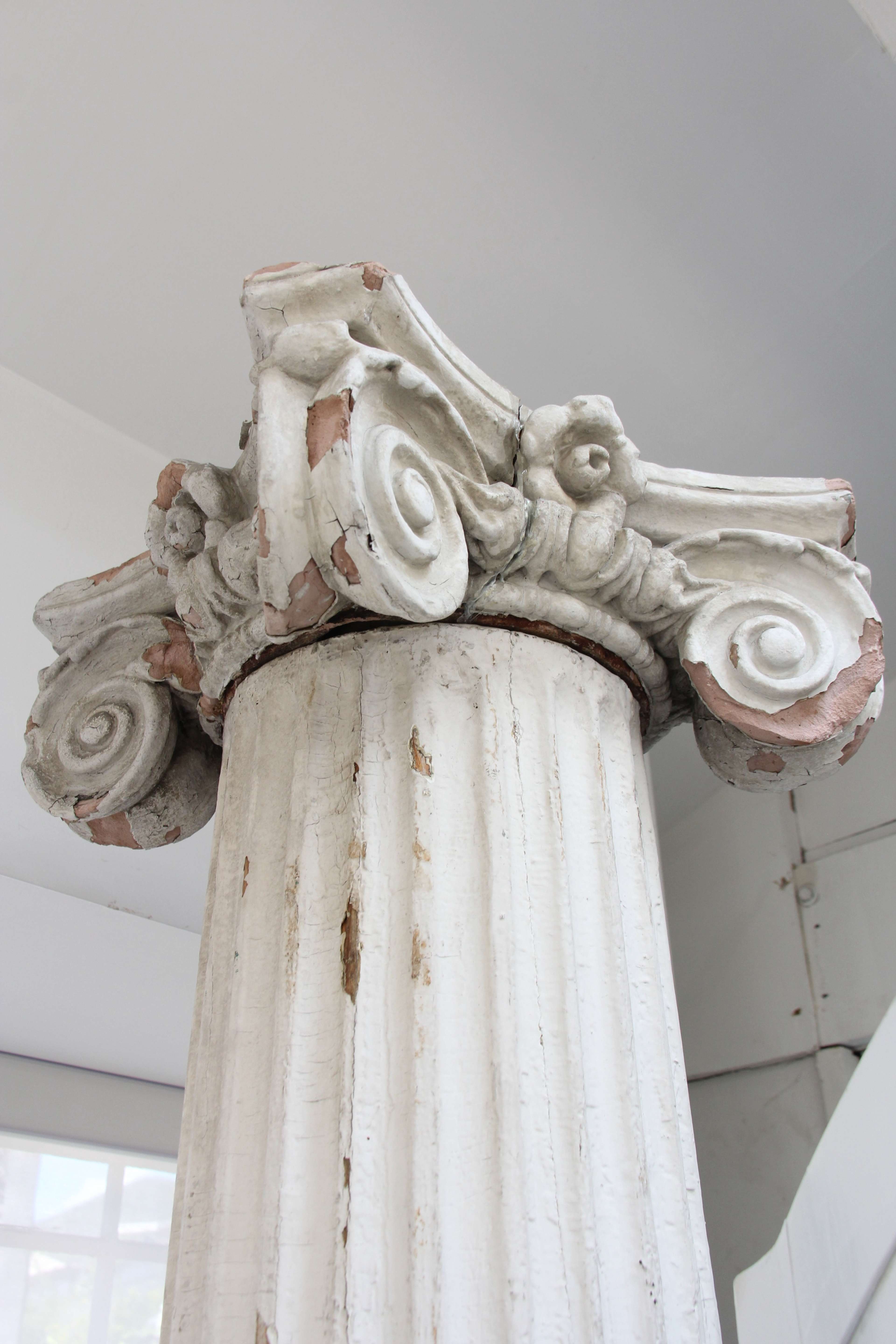 The top of a weathered white column featuring ornate scroll-shaped carvings.