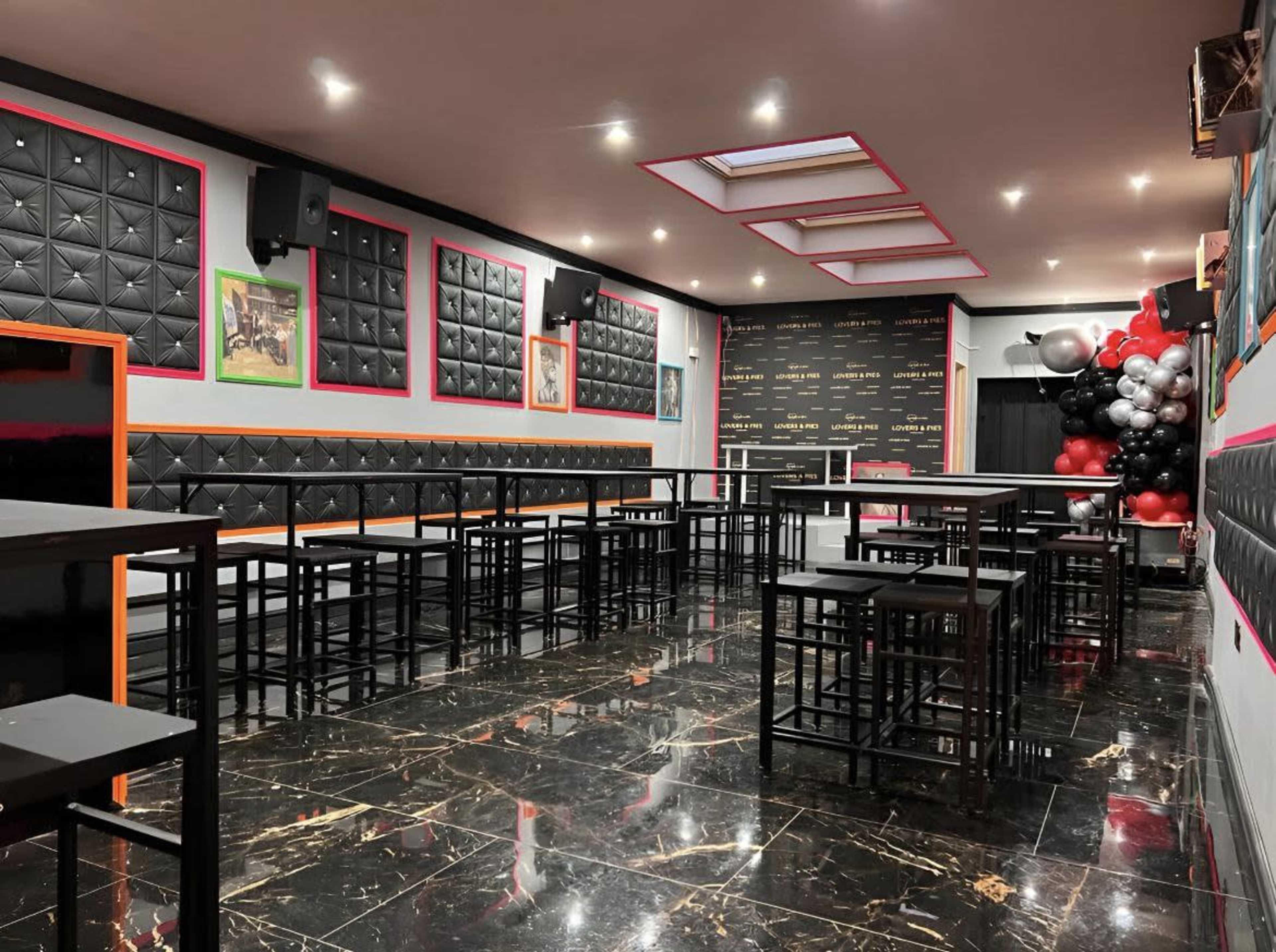 A modern event space with black leathered walls, high tables, and a decorative balloon arrangement in the corner.