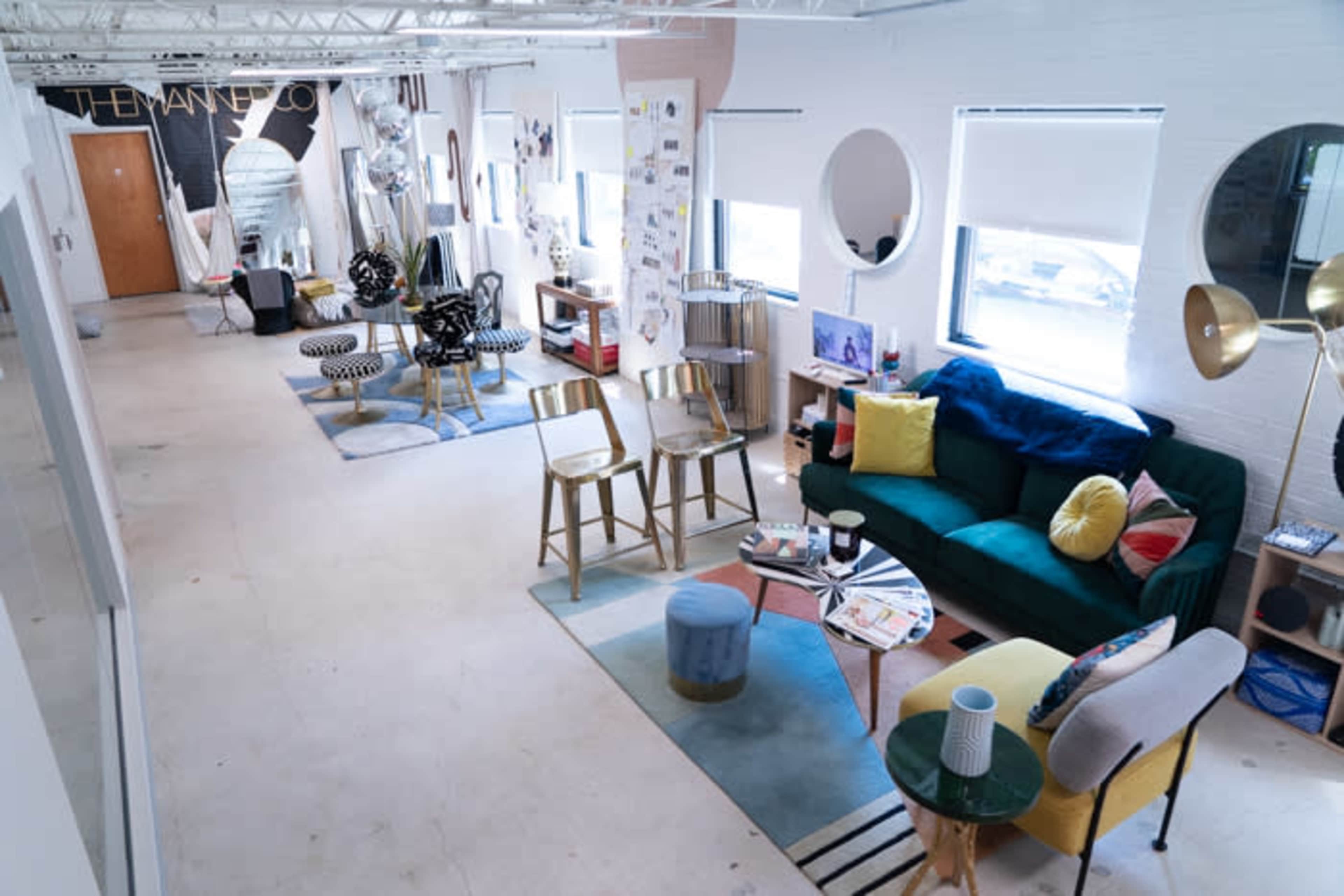 The image shows a spacious, modern office or studio interior featuring various seating areas, decorative items, and artwork on the walls.