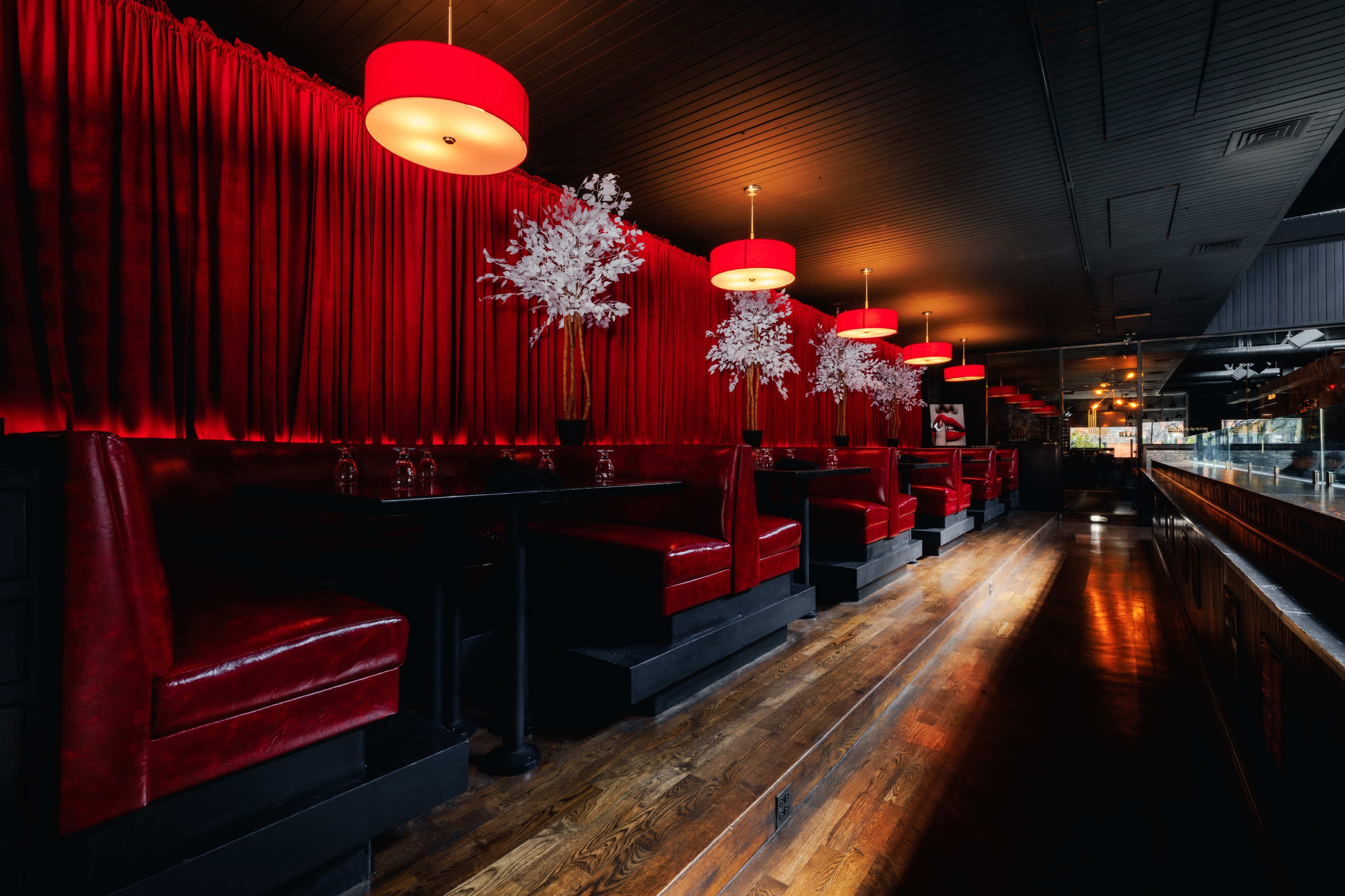 The image shows a dimly lit restaurant with red velvet booths, red lamps, and decorative white flowers against a red curtain backdrop.