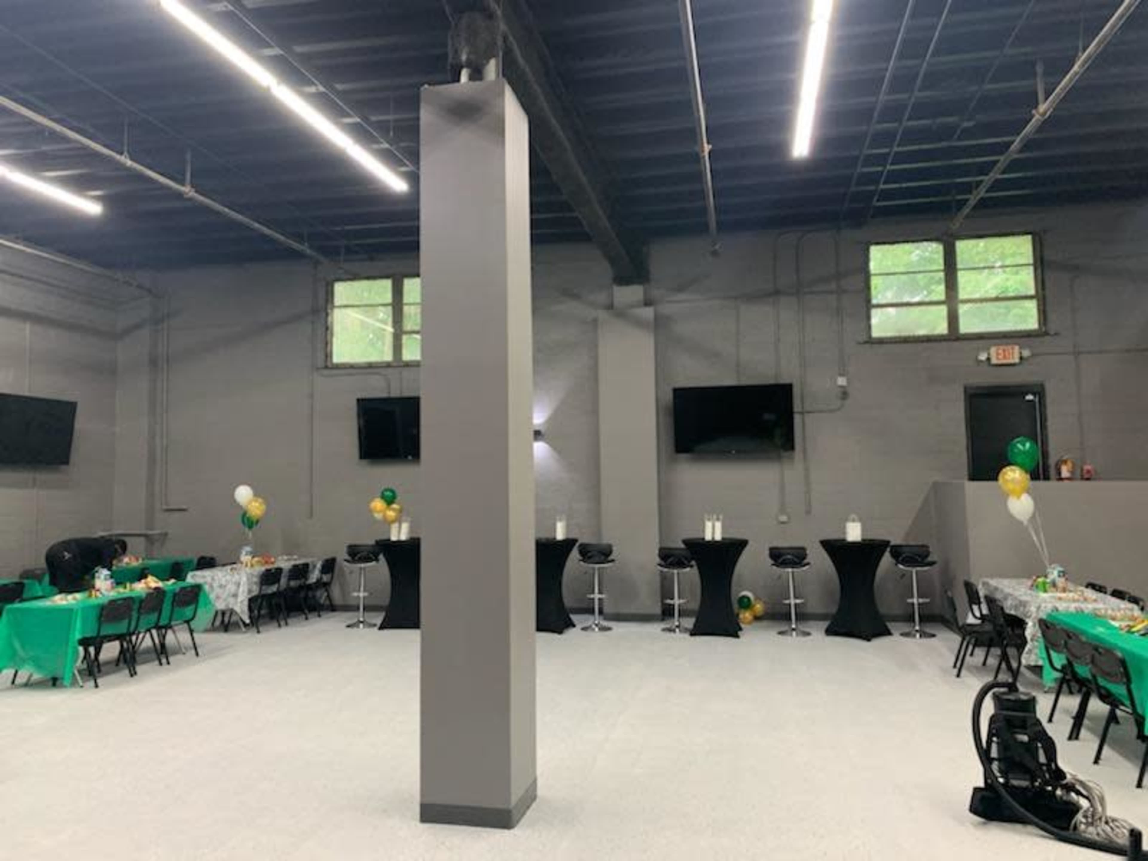A spacious event room with tables covered in green cloth, high-top black tables, and televisions mounted on the walls.