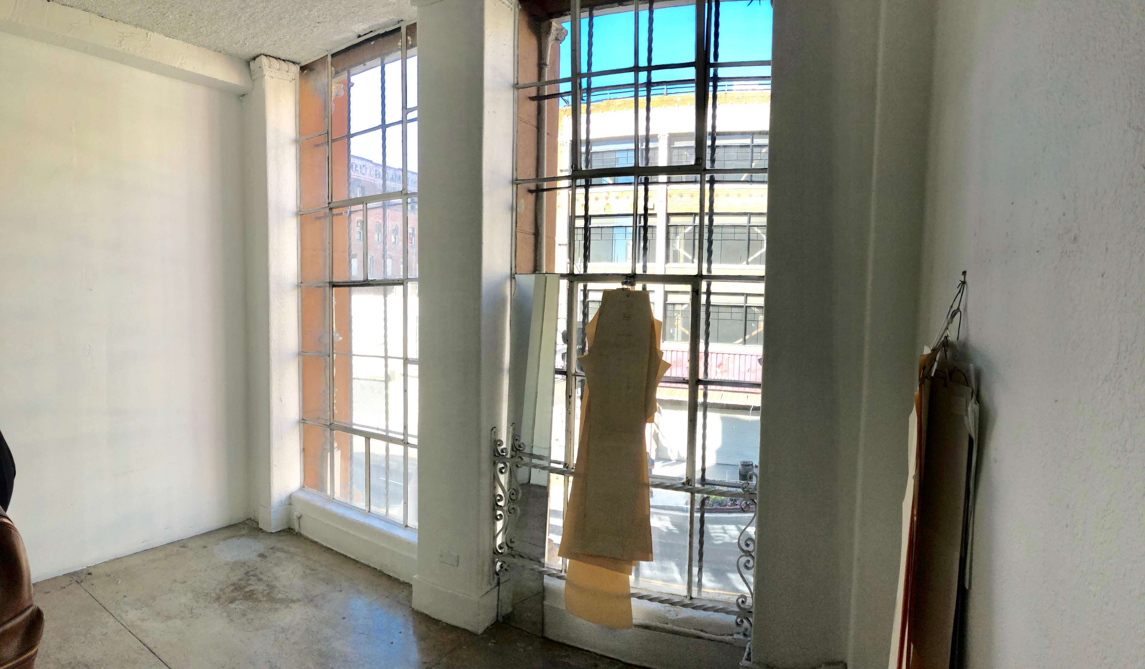 A spacious room with large, barred windows allowing light to enter, revealing a view of the street outside.