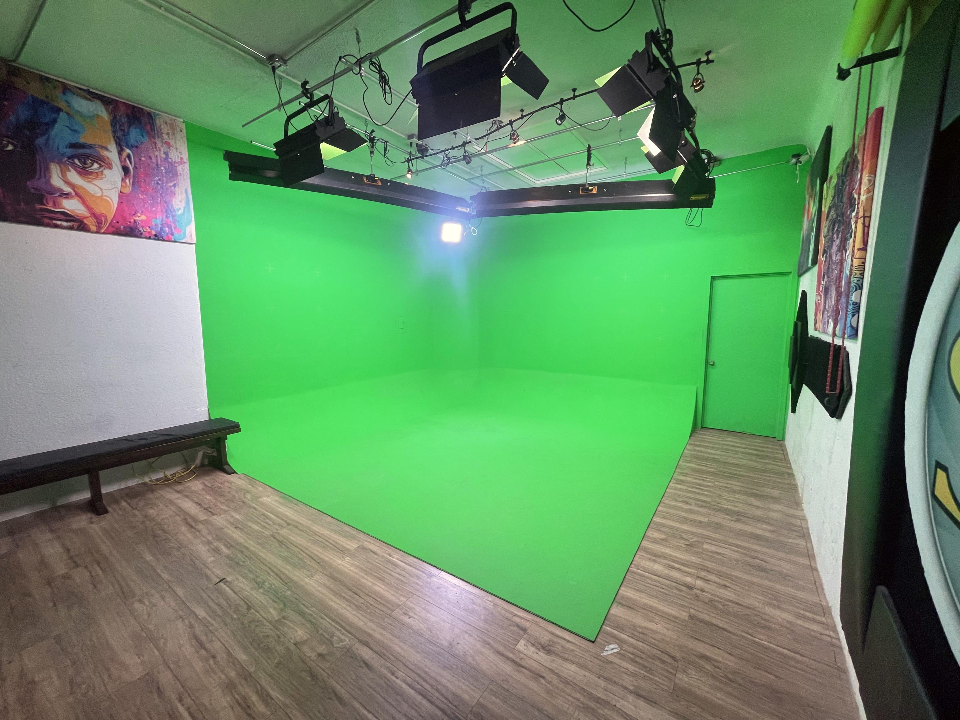 A green-screen studio with a wooden bench, bright lights overhead, and a mural on the wall.