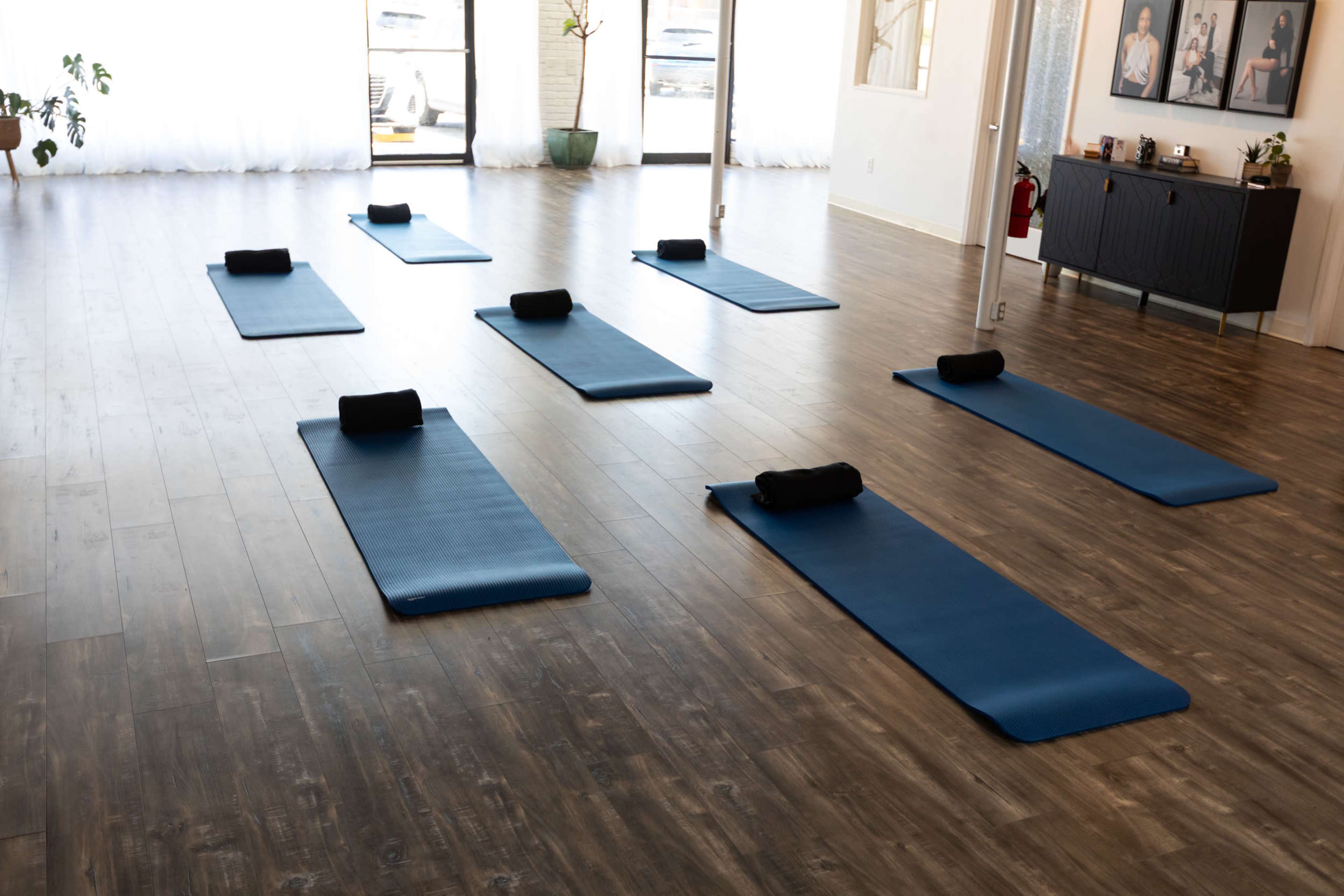 The image shows a spacious yoga studio with several blue mats arranged neatly on a wooden floor.
