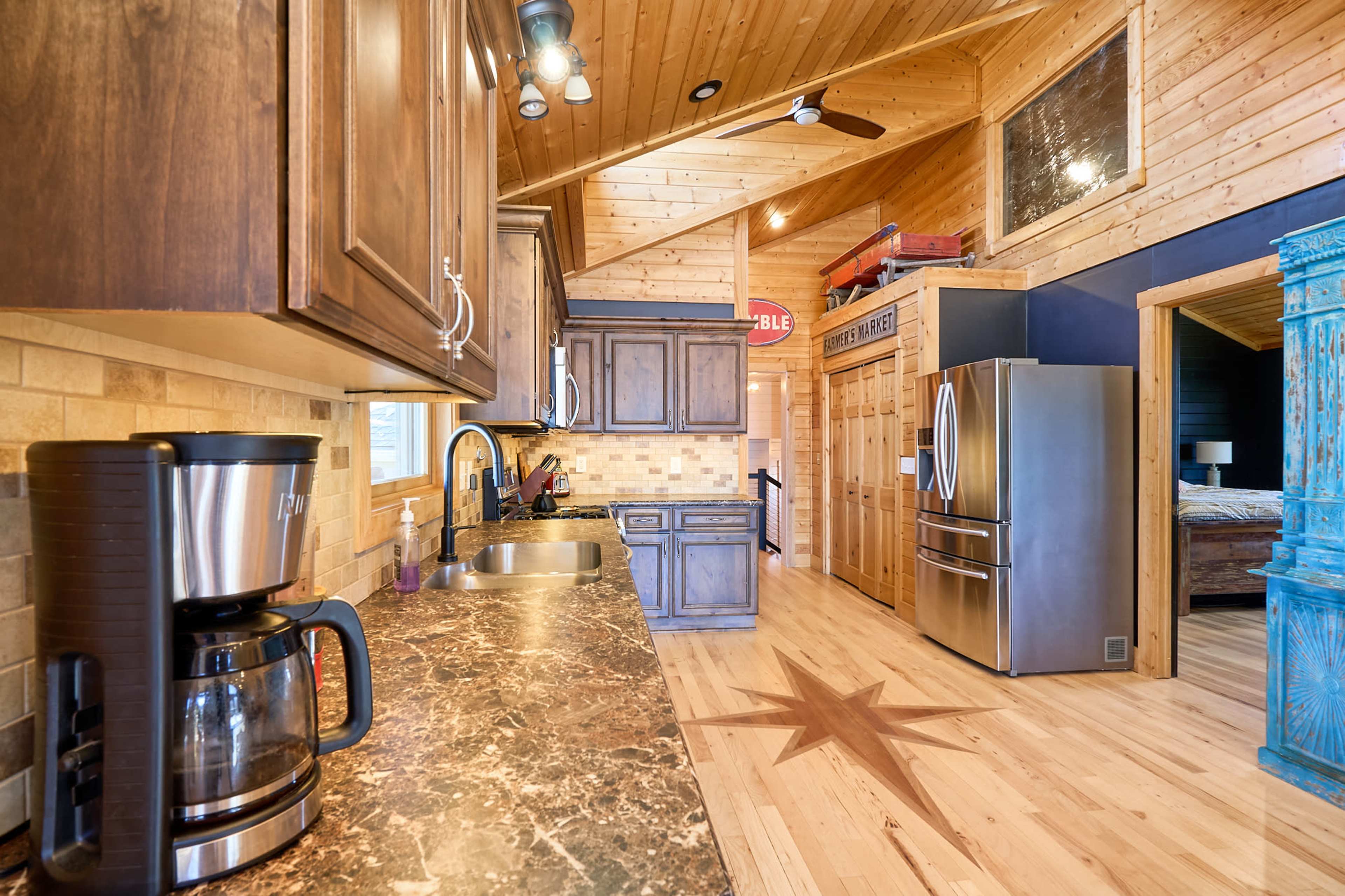 The image shows a modern kitchen with wooden cabinetry, a granite countertop, and stainless steel appliances, featuring a coffee maker and a decorative star on the floor.