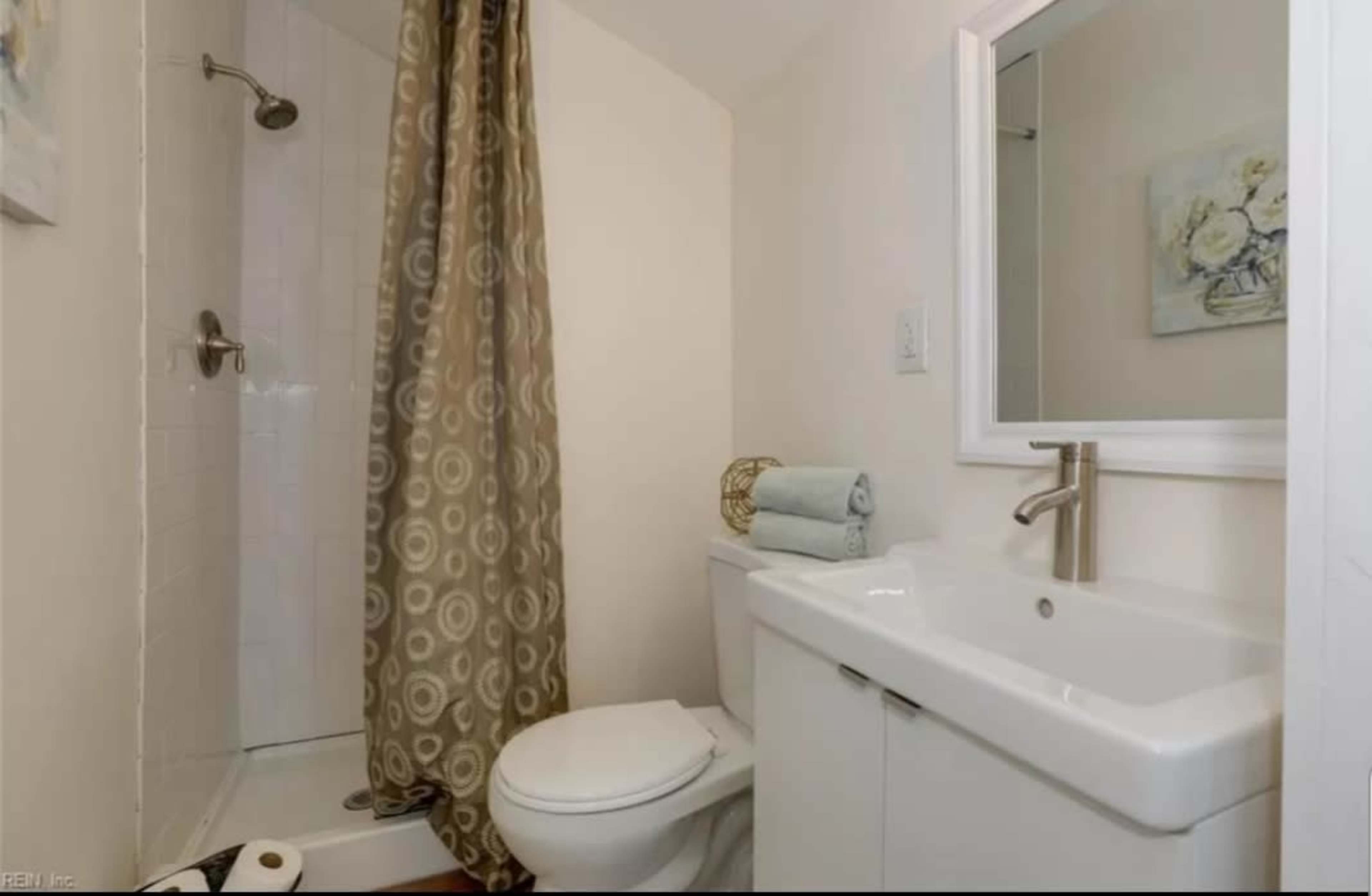 A small bathroom featuring a shower with a curtain, a toilet, and a vanity with a sink and mirror.