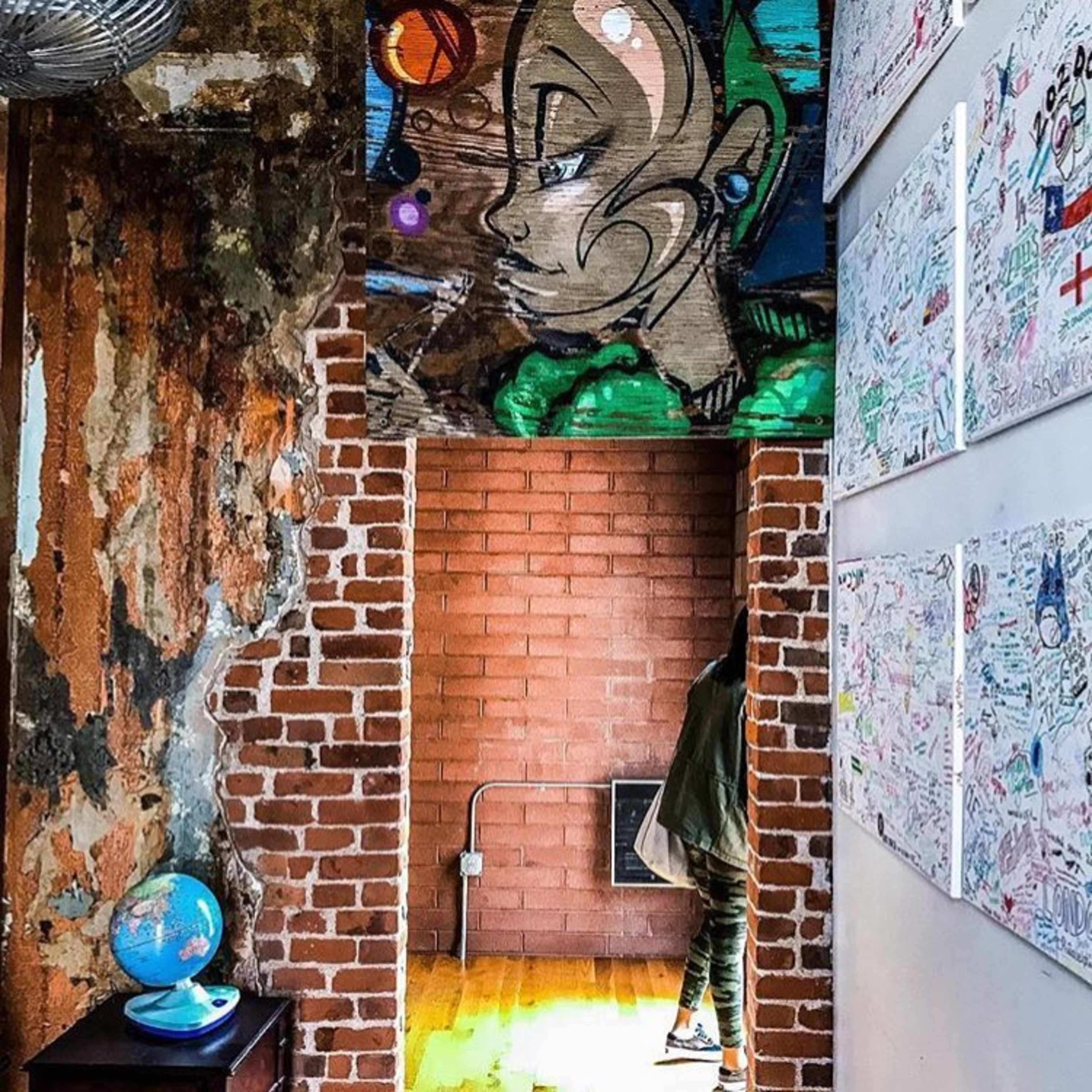 A corridor transitioning from exposed brick and peeling wall paint to colorful artwork and decorative drawings on paper.