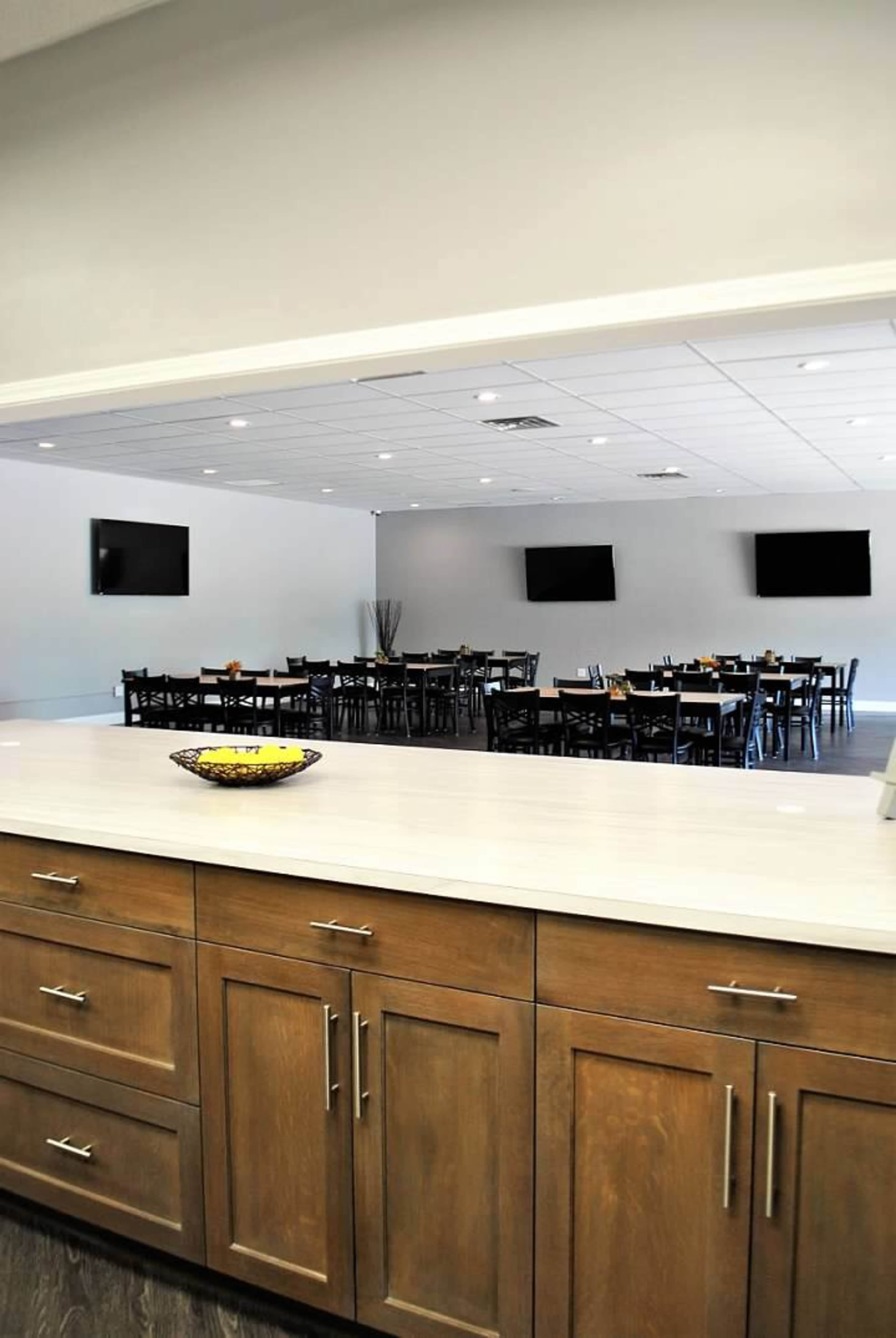 A spacious dining area with multiple tables and chairs set up, visible through a pass-through window from a kitchen or serving area.