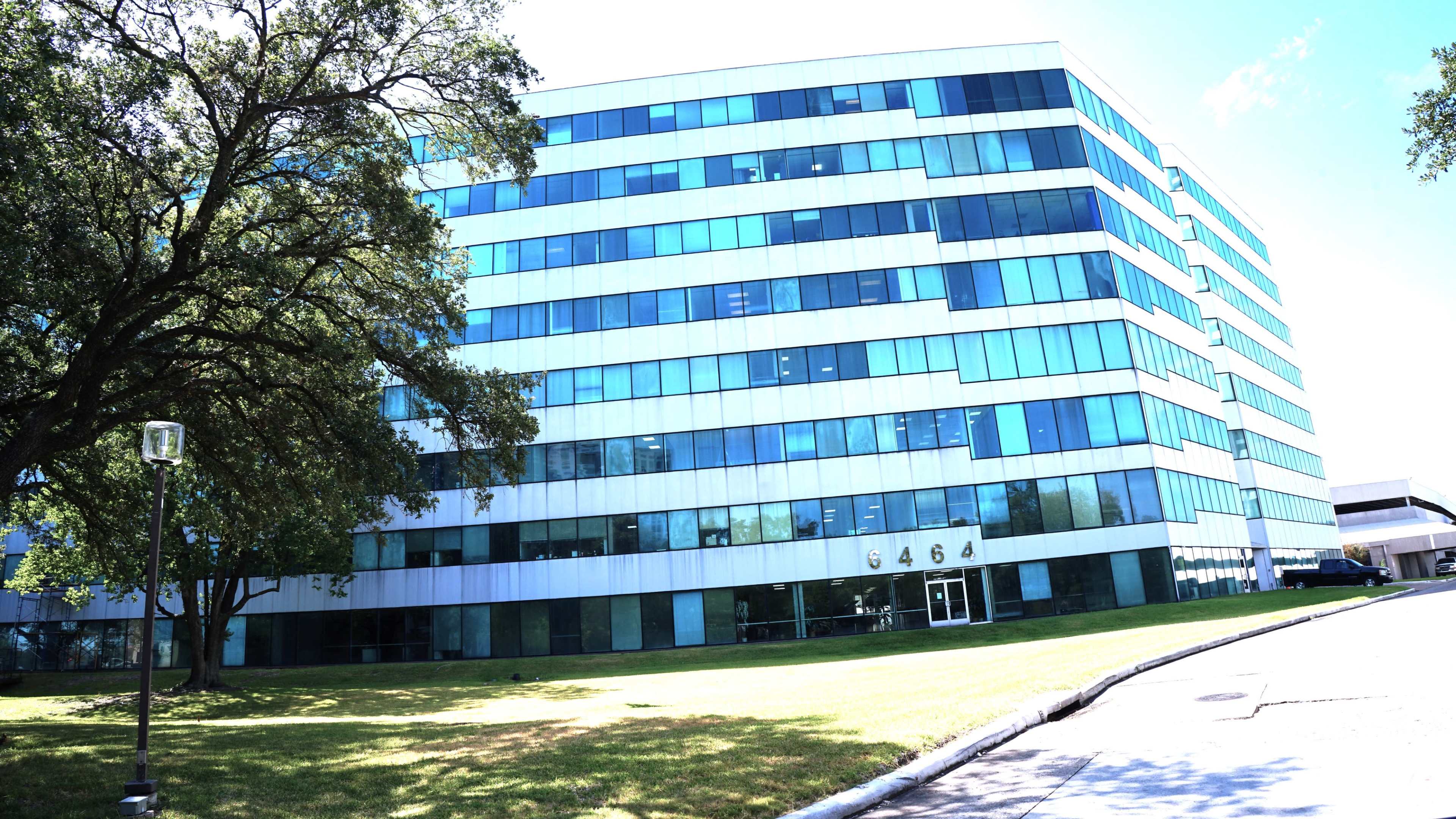 A modern, multi-story office building with large glass windows surrounded by neatly maintained grass and trees.
