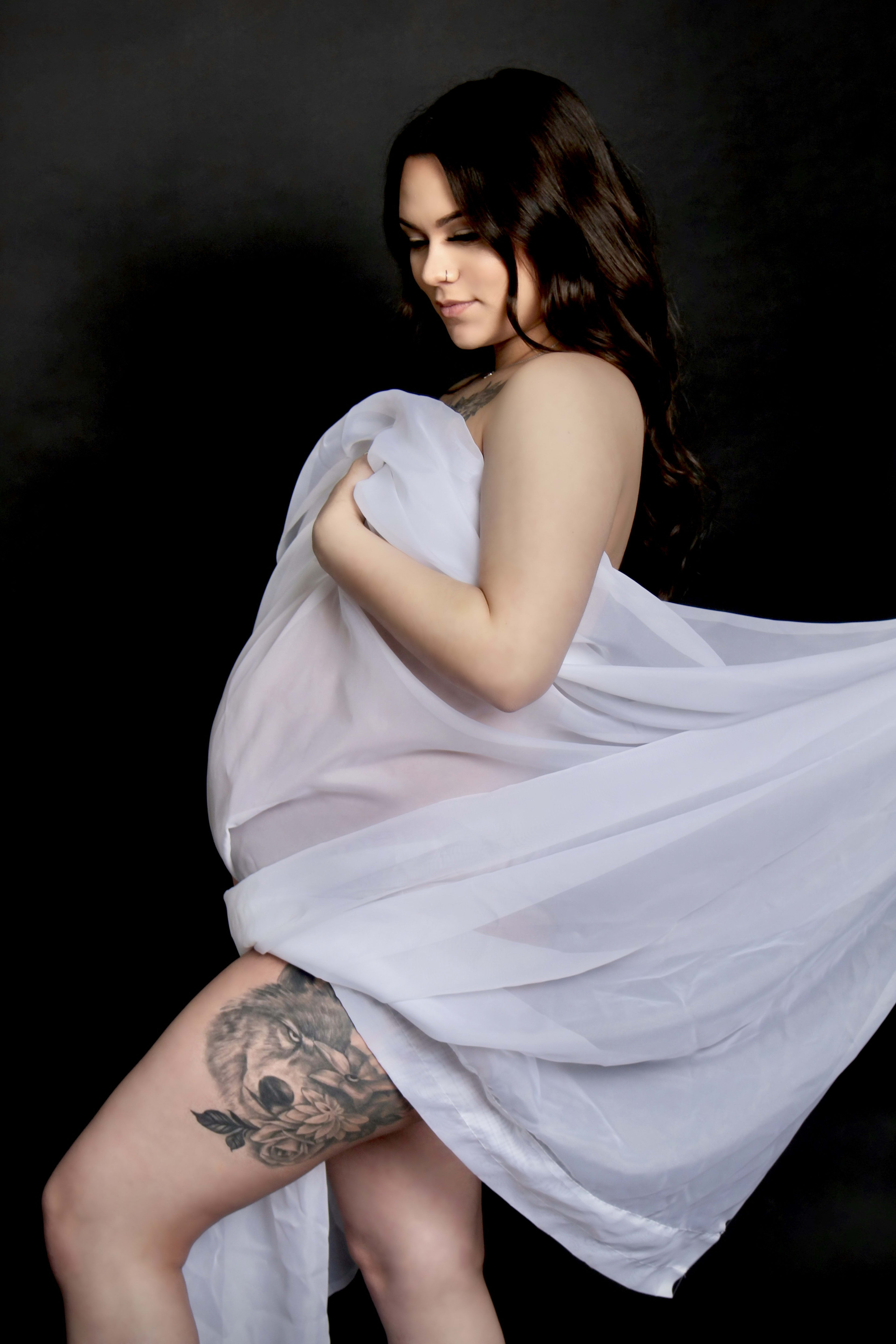 A pregnant woman in a white dress posing for a maternity photo shoot.