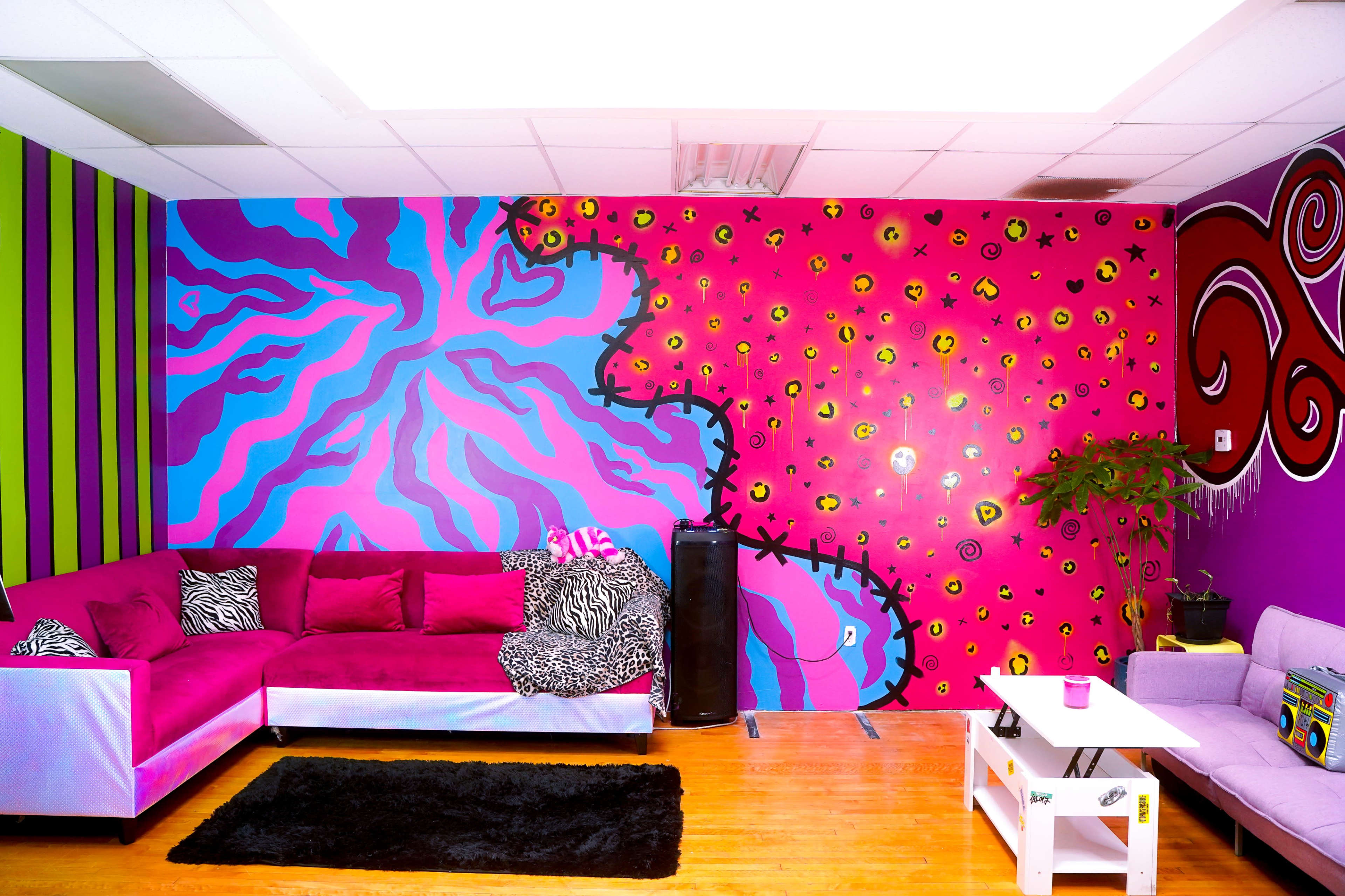 A vibrant lounge area with a pink and purple mural on the wall, a sectional sofa, and a small table on a wooden floor.