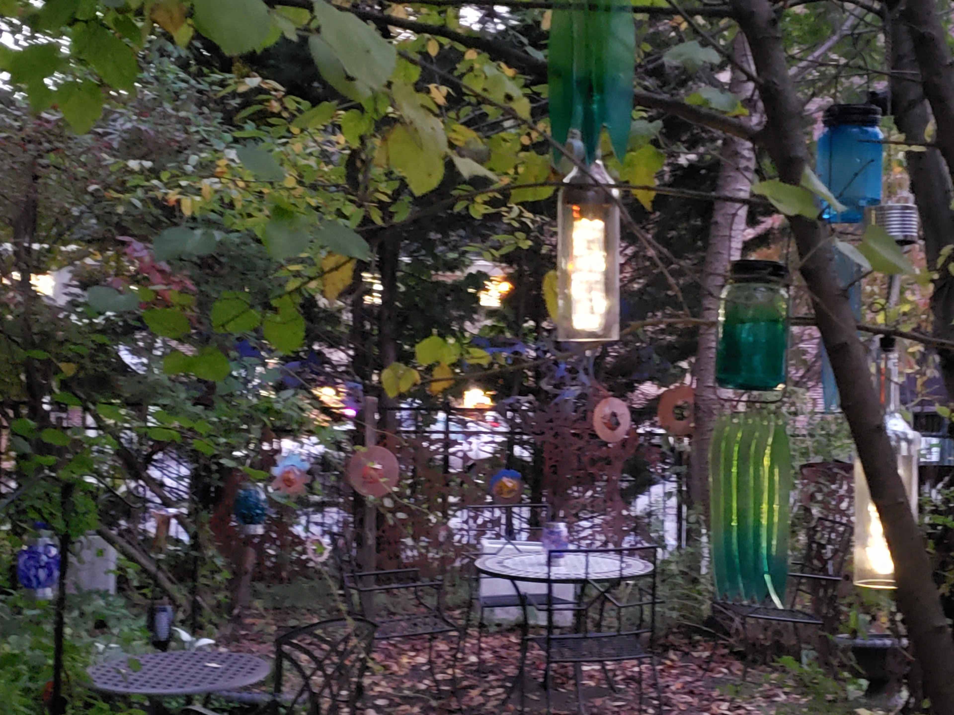 A garden area with metal bistro tables and chairs surrounded by colorful hanging glass jars and autumn leaves.