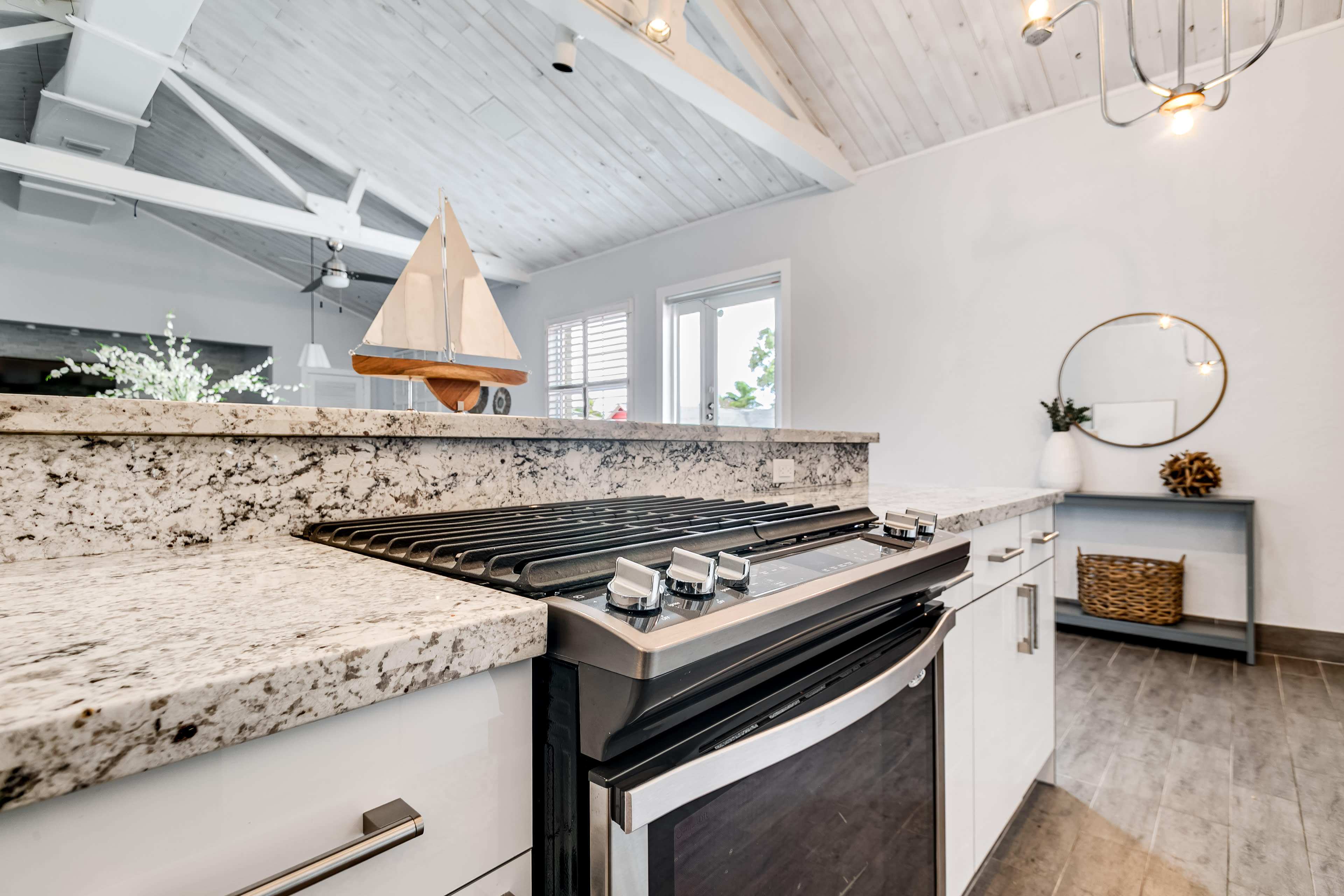 A modern kitchen with a granite countertop, a stainless steel gas stove, and a decorative sailboat on display.