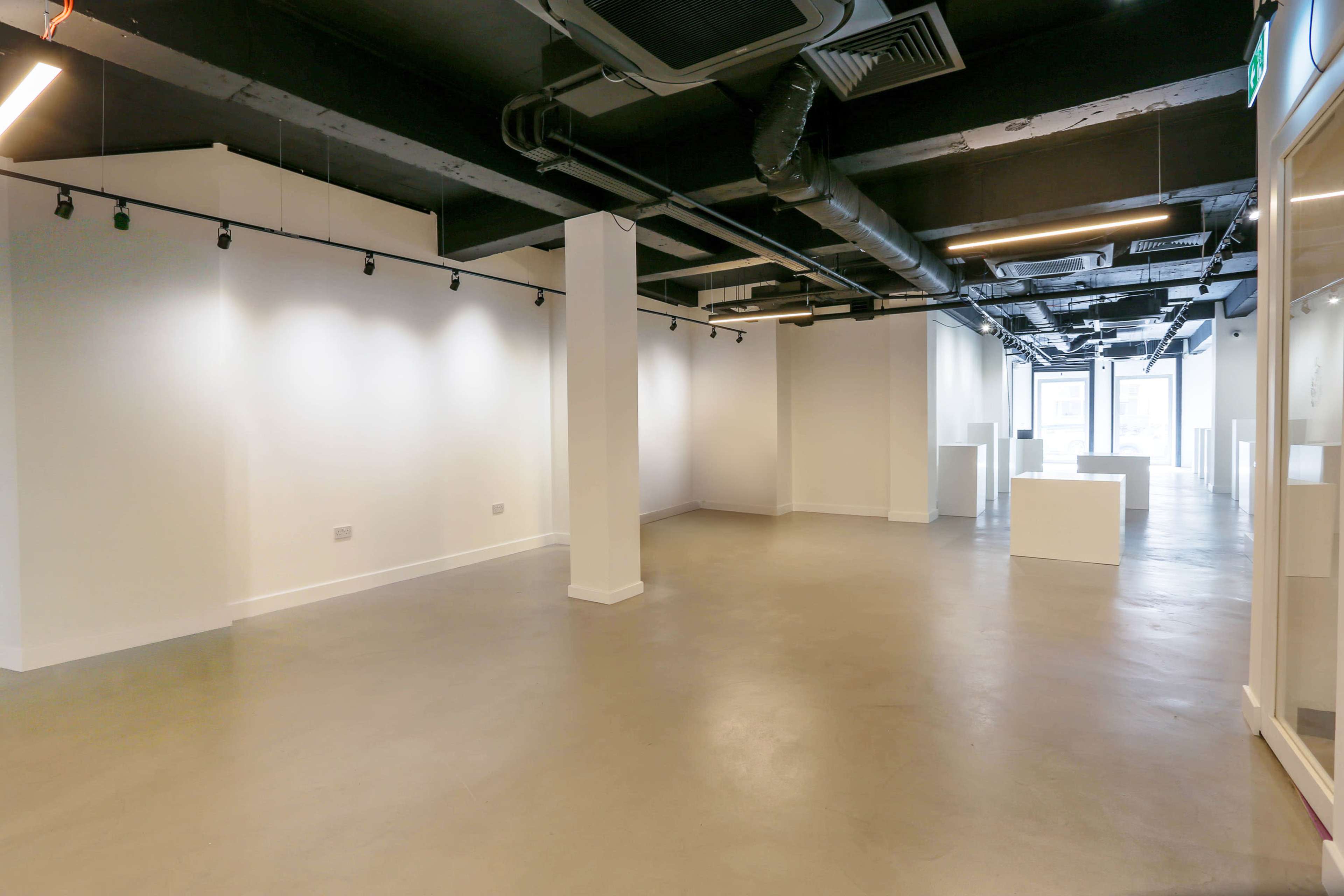 The image shows an empty, modern commercial space with white walls, concrete flooring, and overhead lighting.