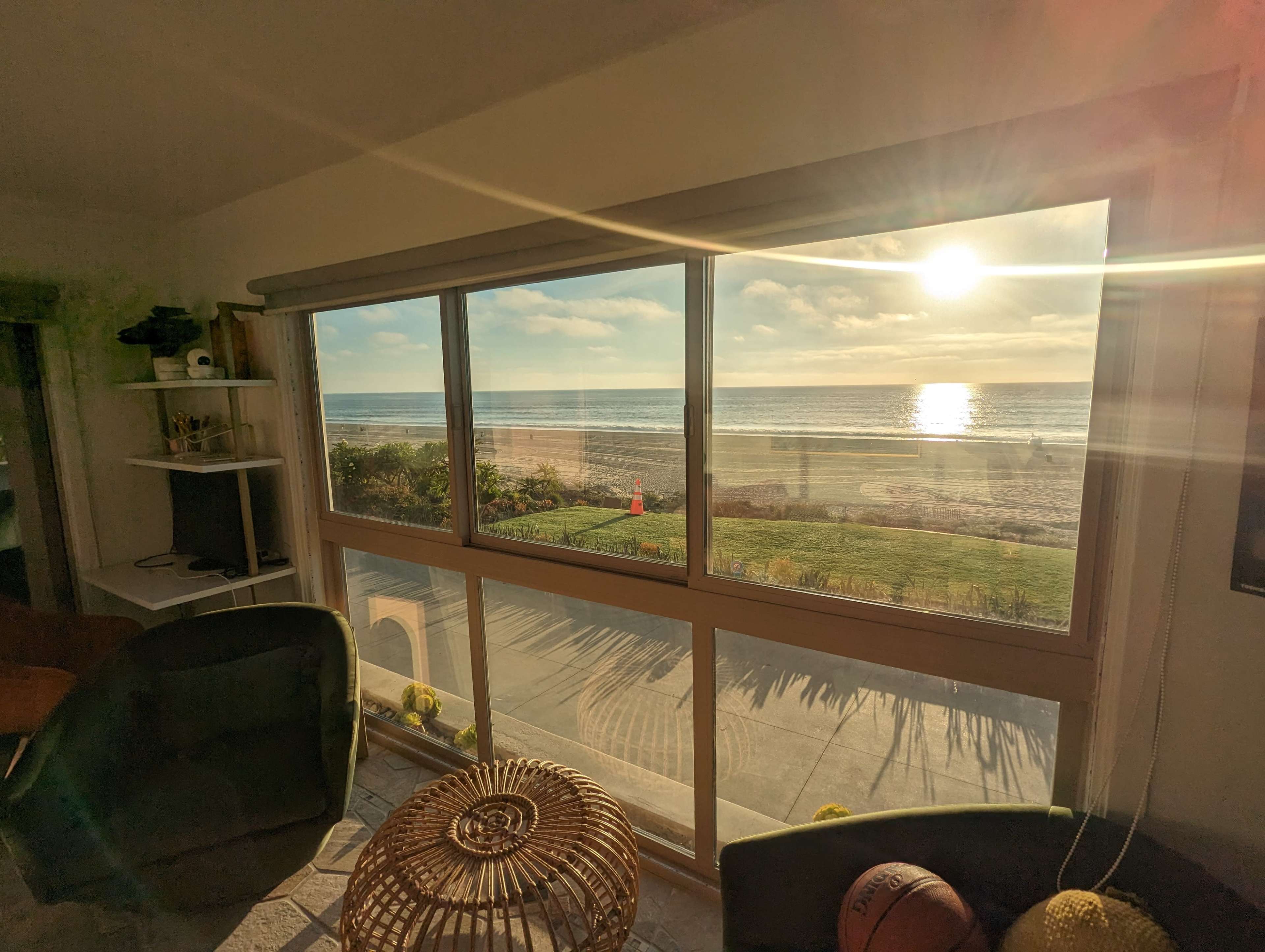 A beachfront view is visible through a large window, showcasing the ocean, a sunlit sky, and a bit of outdoor greenery.