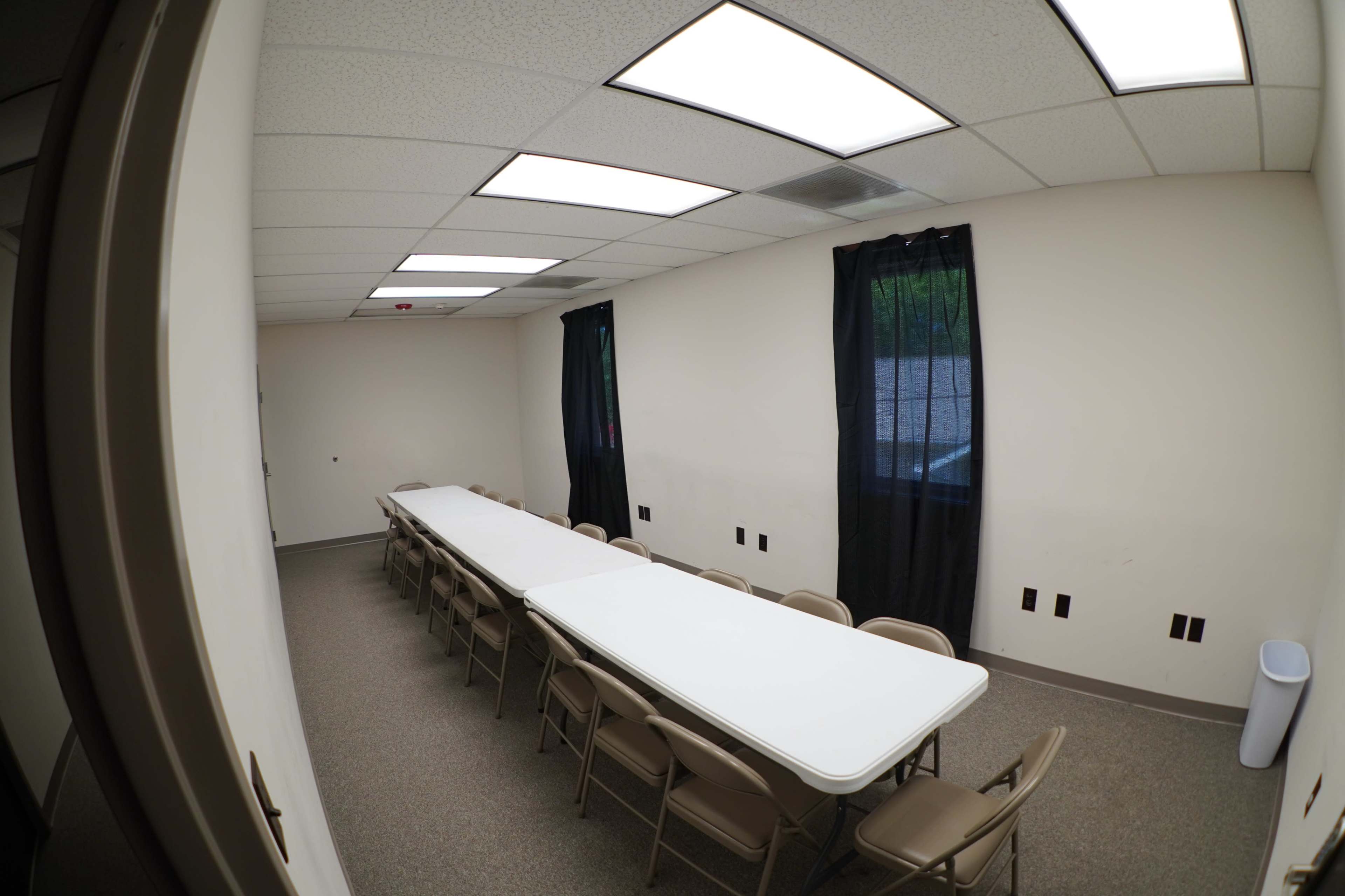 A long table is set up in a well-lit, empty room with black curtains over two windows.