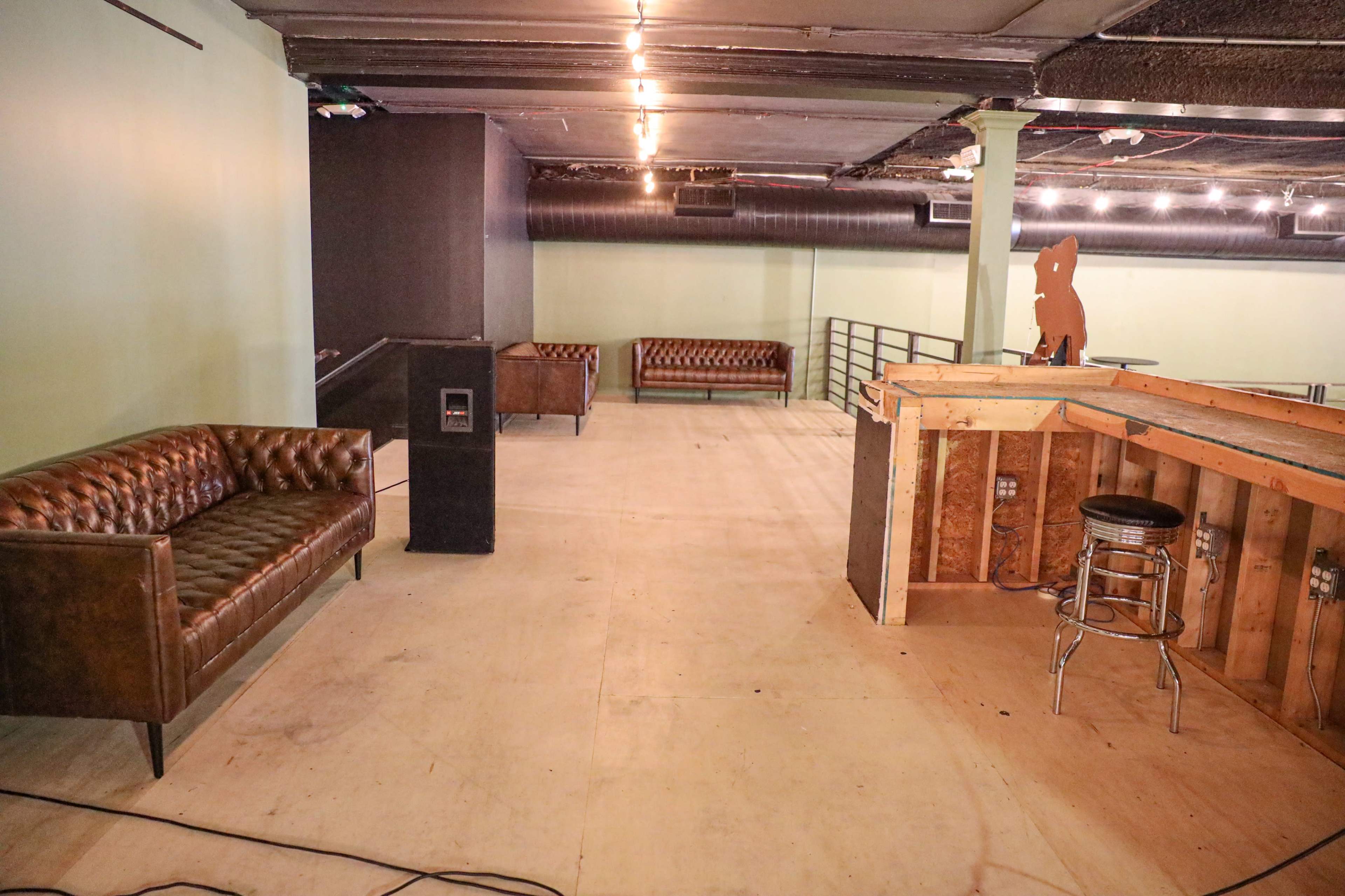 An empty interior space featuring brown leather sofas, a wooden bar structure, and exposed lights on the ceiling.