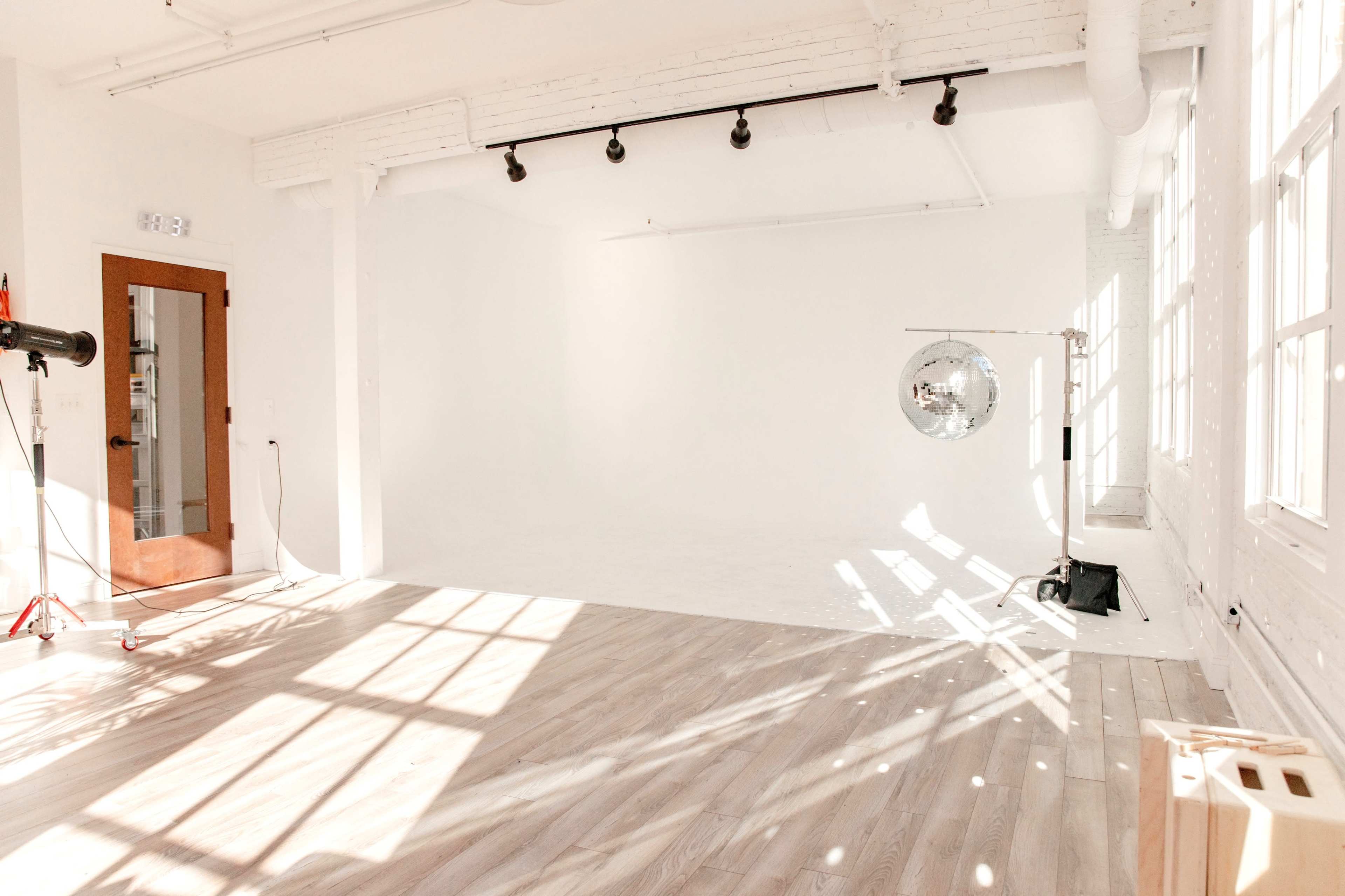 A spacious, well-lit studio with white walls, hardwood flooring, and a disco ball hanging from a stand.